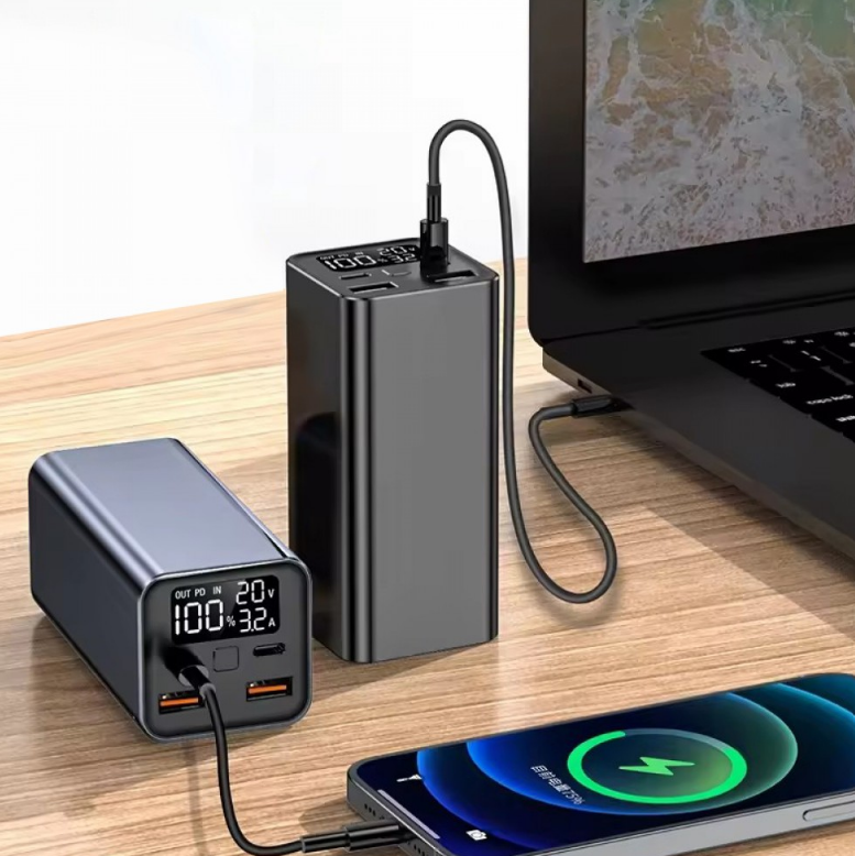 Egy power bank laptopot, telefont és egy másik power bankot tölt. Minden eszköz fa felületen van. Kábelek kötik össze őket.