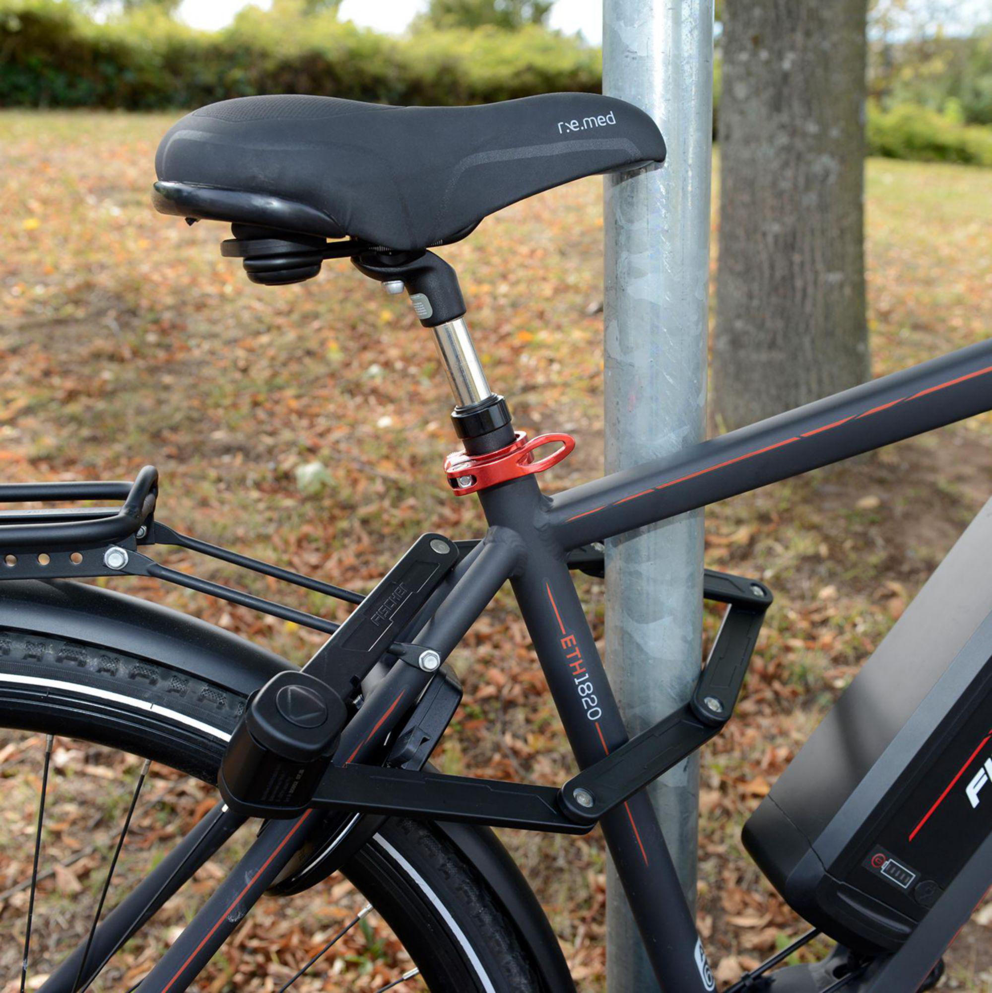 Schwarzes E-Bike, das an einem Pfosten angeschlossen ist. Es hat einen schwarzen Sitz, ein rotes Schloss und einen schwarzen Rahmen mit roten Details.