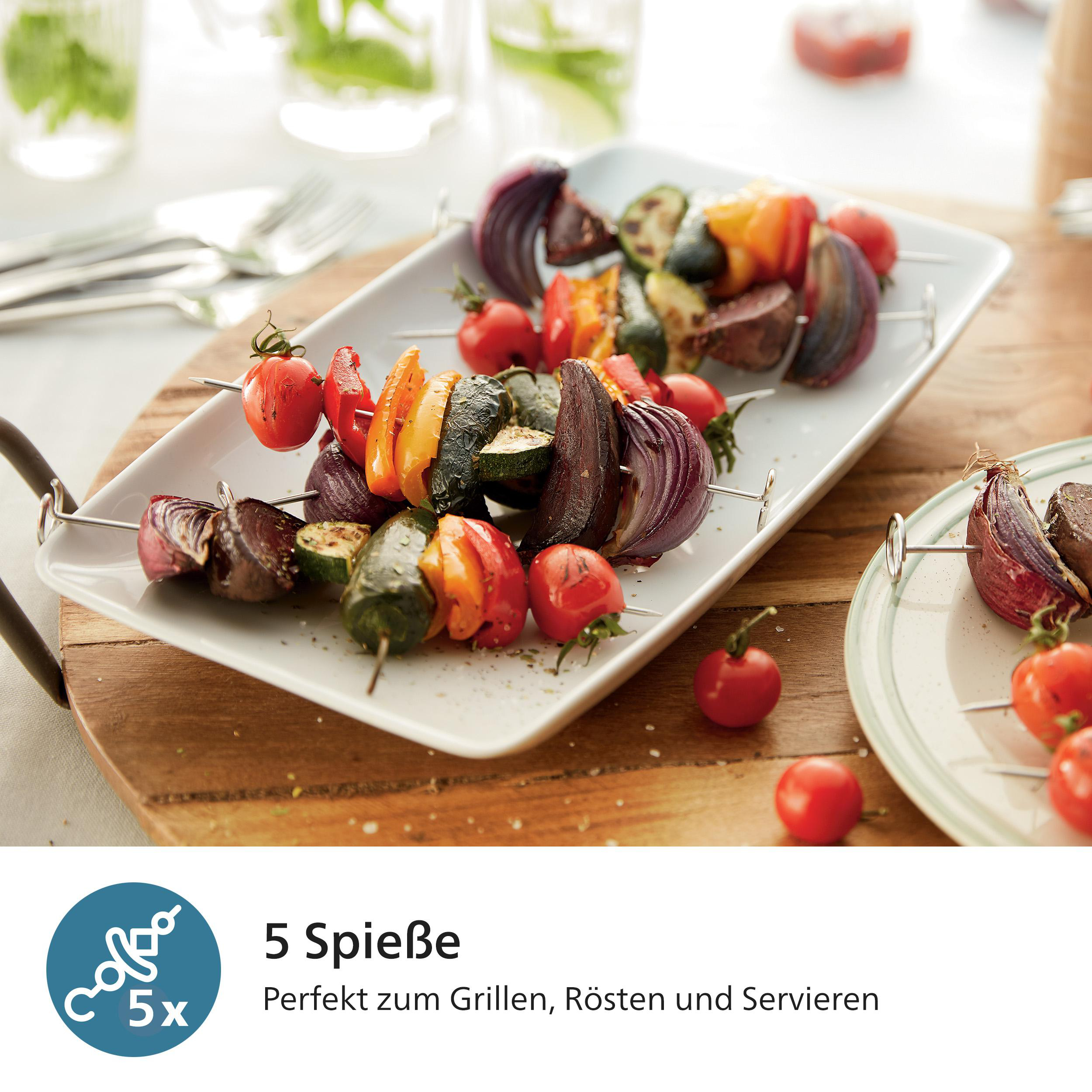 Gegrillte Gemüsespieße auf einem weißen Teller. Tomaten, Paprika, Zucchini und Zwiebeln sind sichtbar. Holzbrett und Gläser im Hintergrund.