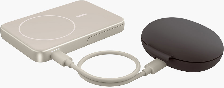 Un chargeur sans fil beige clair est connecté à un étui d'écouteurs gris foncé via un câble beige clair.