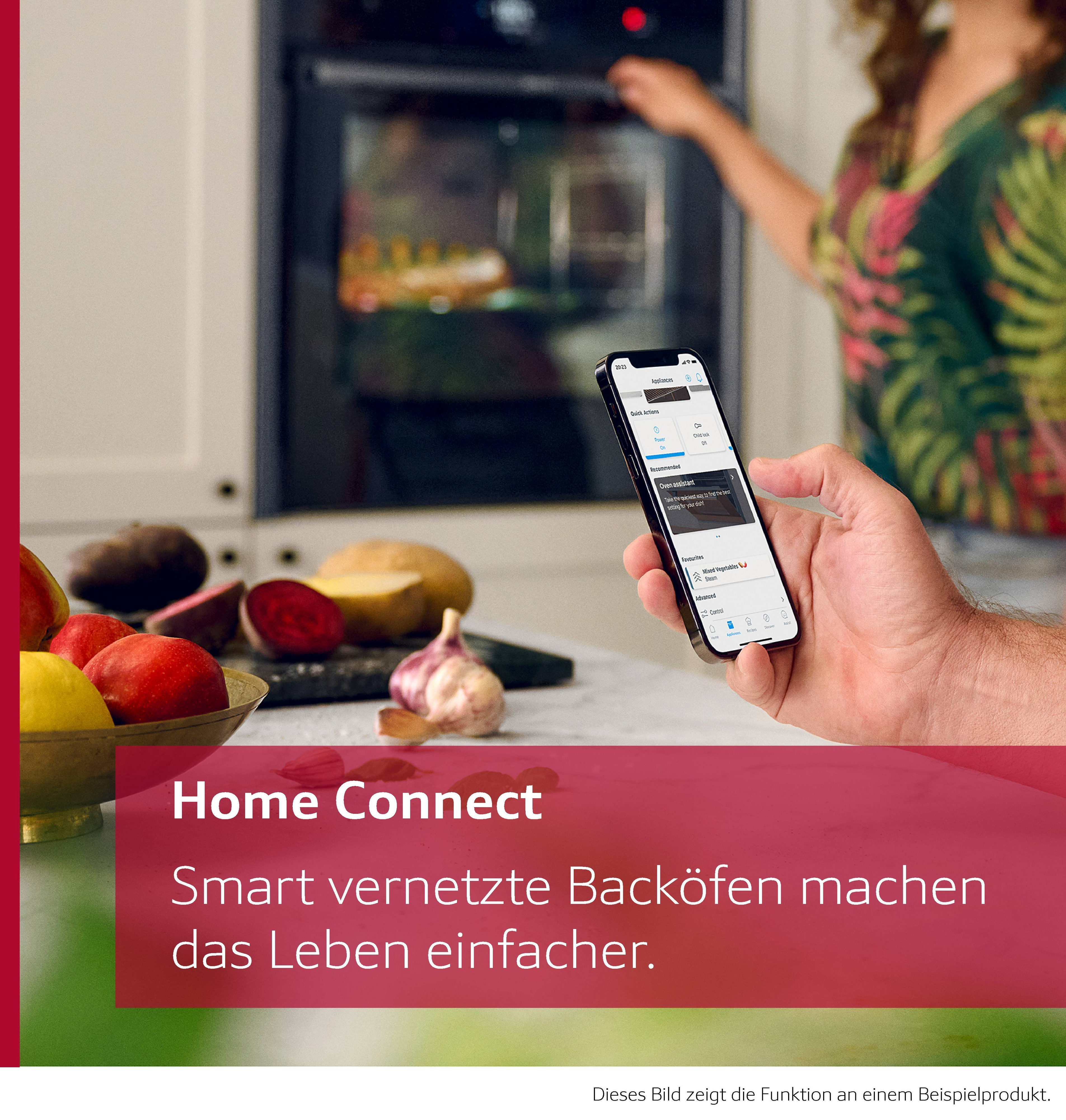 Eine Hand hält ein Telefon mit einer Ofensteuerungs-App. Gemüse und Obst liegen auf der Theke. Eine Person steht am Ofen.