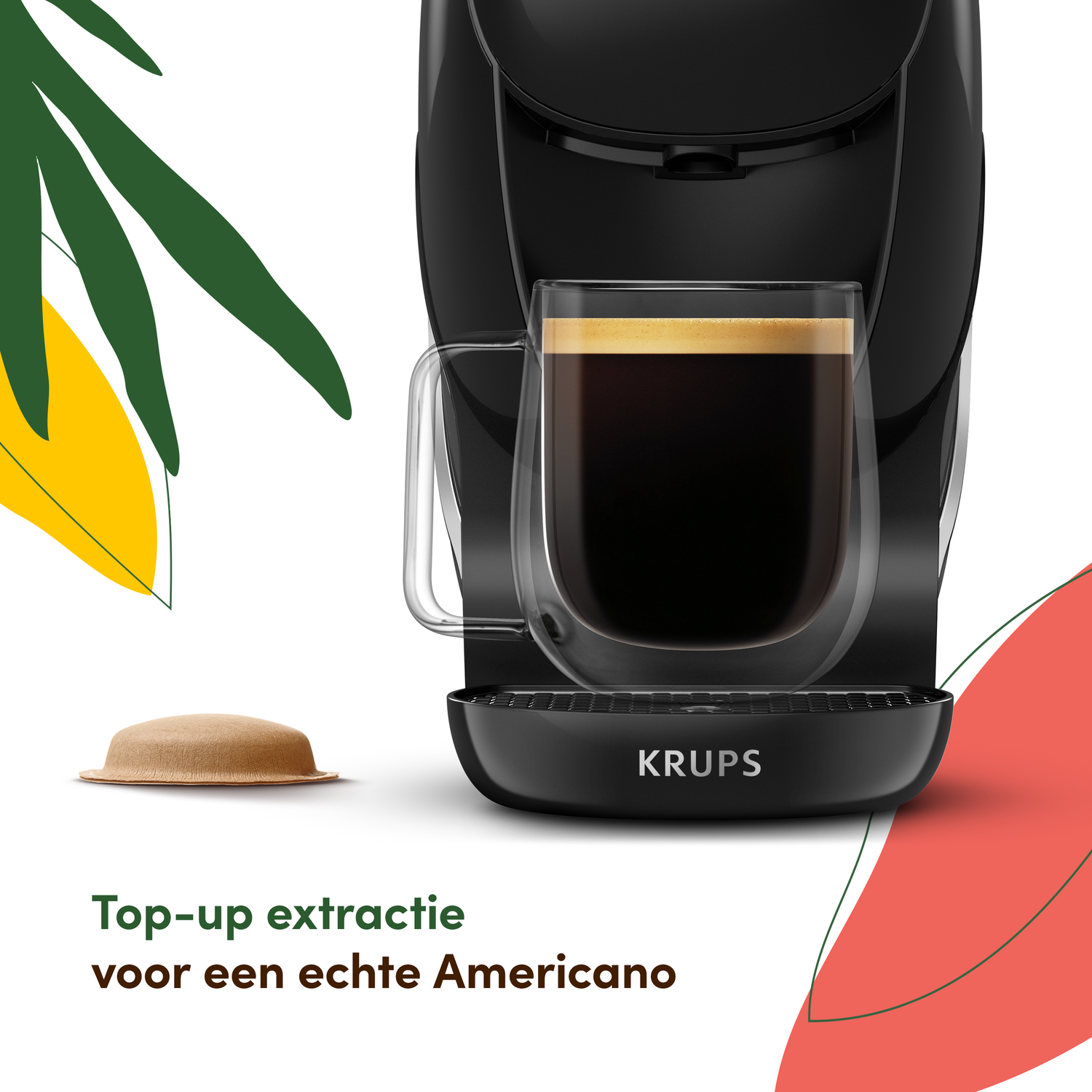 Black Krups coffee machine with a glass of coffee. A coffee pod is on the left. Green and yellow leaves in the background.