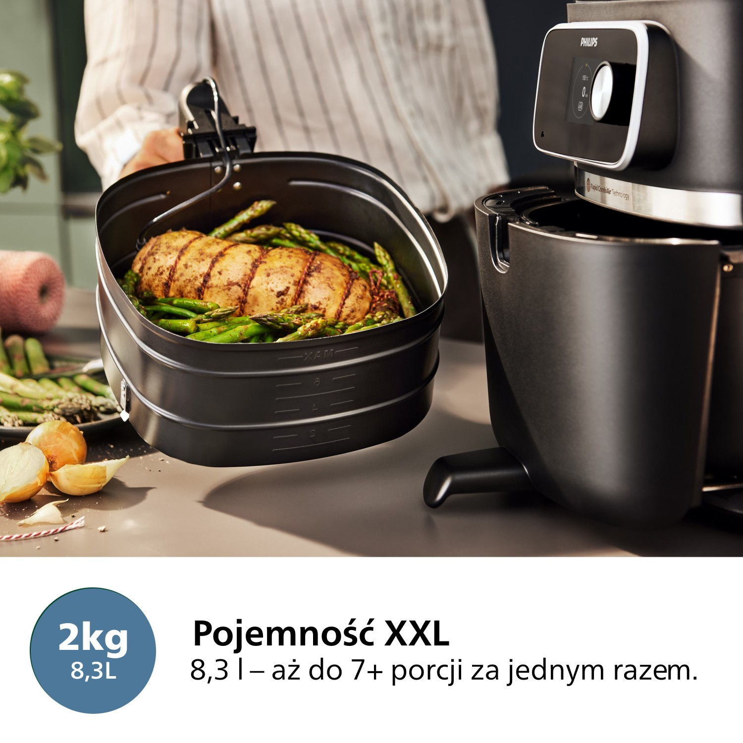 Frytownica powietrzna z jedzeniem w środku i osoba trzymająca kosz. Cebula i szparagi na pierwszym planie. Frytownica jest czarna.