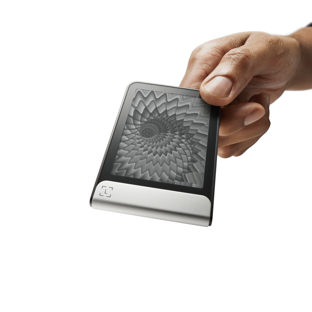 Una mano sostiene un dispositivo digital. La pantalla muestra un patrón en espiral. El dispositivo tiene una base plateada y una pantalla negra.