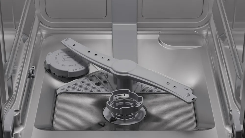 Wnętrze zmywarki. Widoczne ramię natryskowe i filtr. Wnętrze jest metalicznie szare.