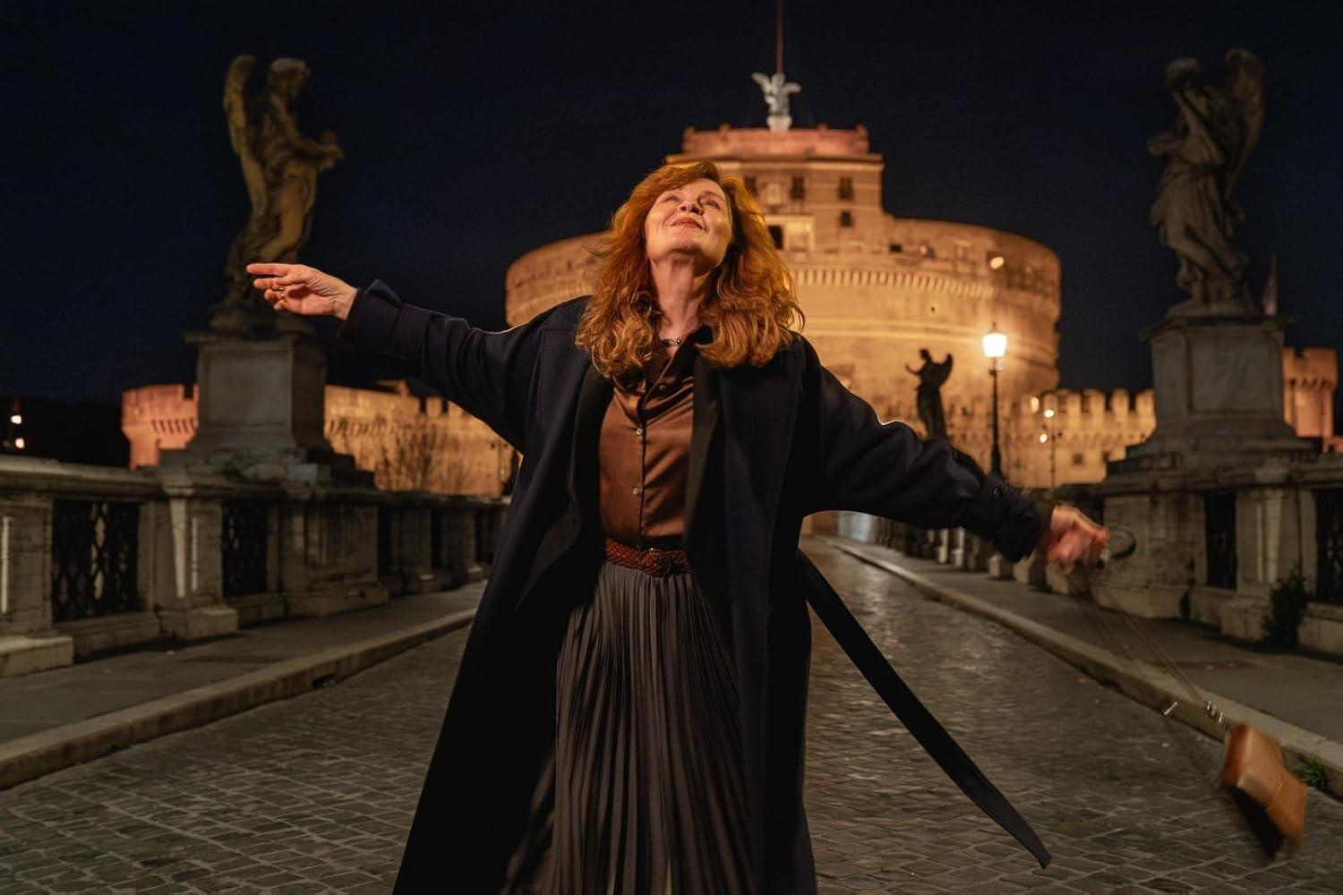 Frau mit ausgestreckten Armen auf einer Brücke bei Nacht, mit einem Schloss im Hintergrund. Auf beiden Seiten stehen Engelsstatuen.