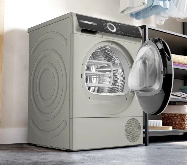 Beżowa suszarka z otwartymi drzwiami. W środku widoczny metalowy bęben i półki. Po prawej półka z przedmiotami.