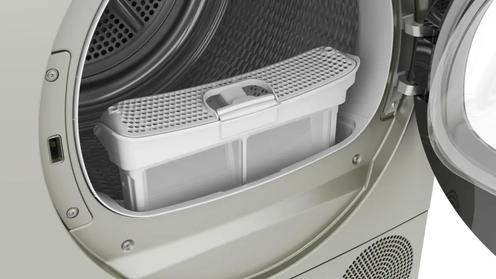 Zbliżenie suszarki z otwartymi drzwiami. Widoczny jest biały filtr na kurz. Wnętrze suszarki jest szare.