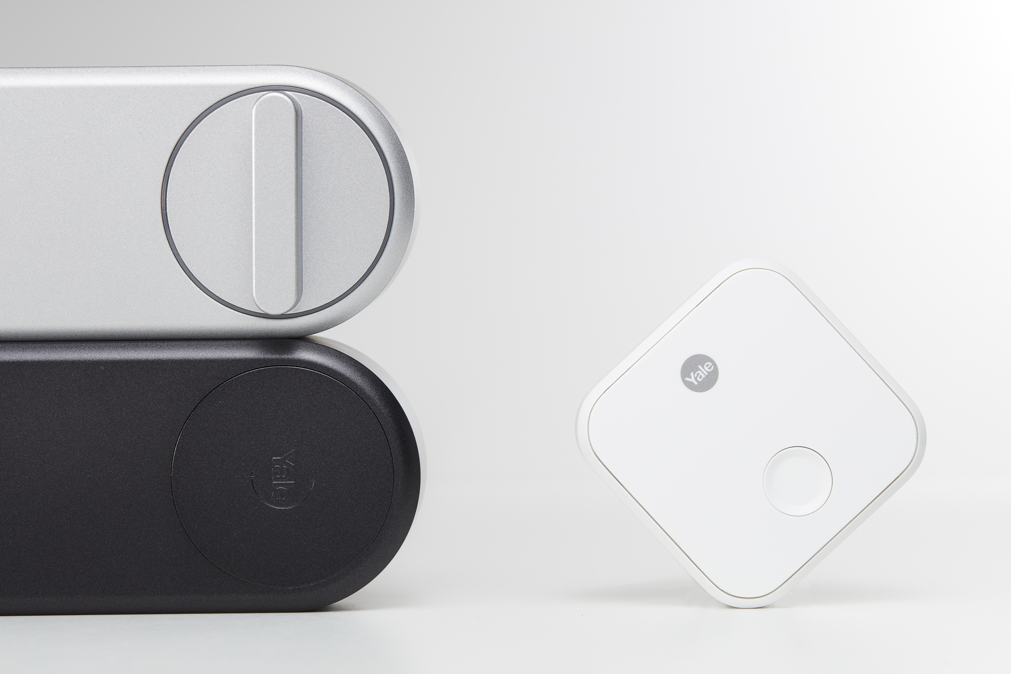 Ein silbernes und schwarzes Yale Smart Lock und ein weißes Yale-Gerät auf weißem Hintergrund. Das Schloss besteht aus zwei Teilen.