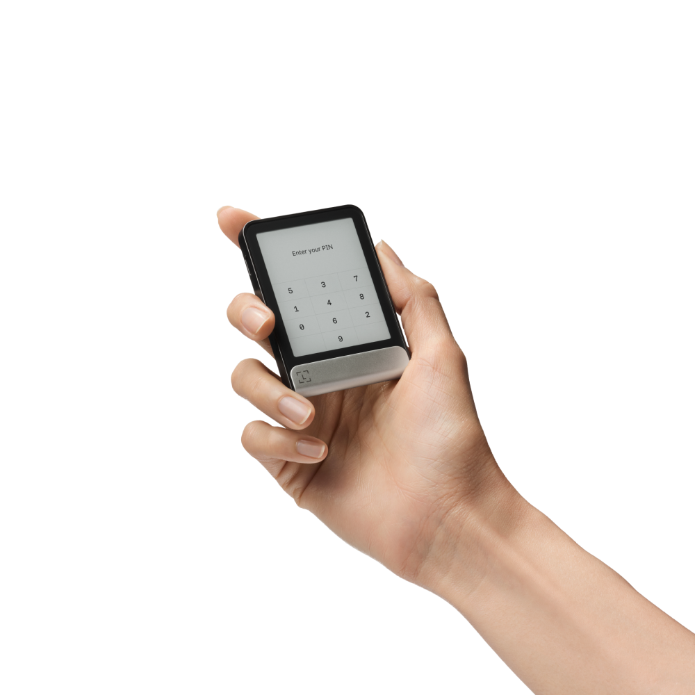 Una mano sostiene un dispositivo negro con una pantalla que muestra un teclado de entrada de PIN. La pantalla dice "Enter your PIN".
