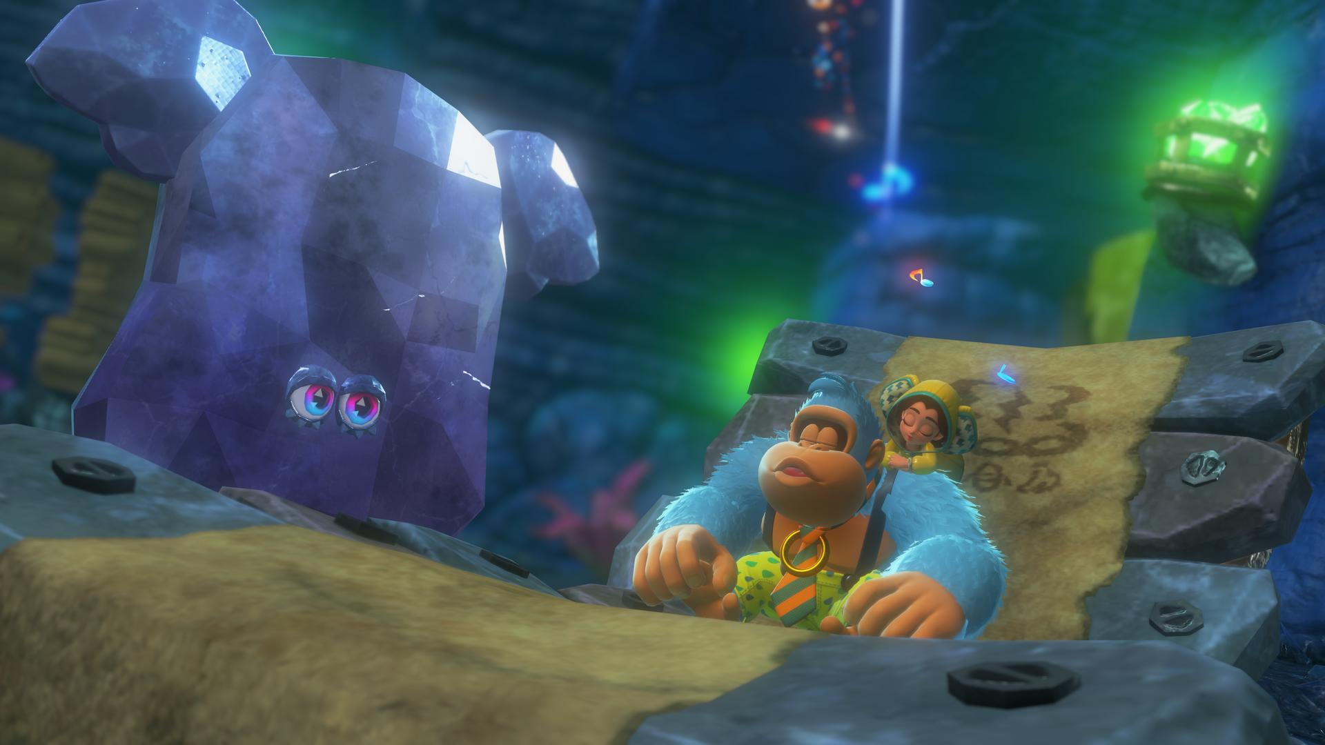 Donkey Kong mit einem Charakter neben einem großen, blauen Kristall. Sie befinden sich auf einer Steinplattform. Der Hintergrund ist eine Höhle.