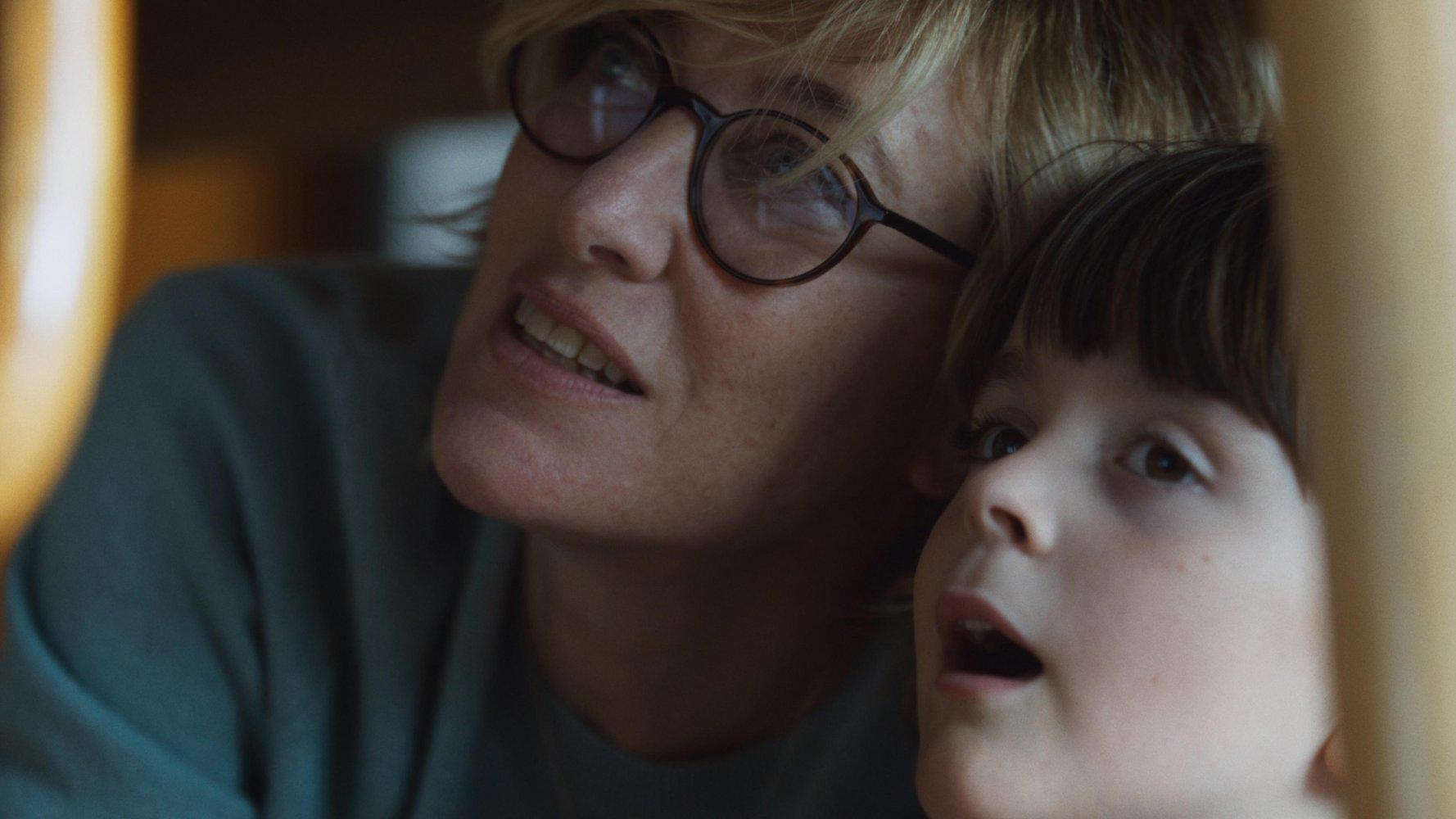 Eine Frau mit Brille und ein Kind mit offenem Mund blicken nach oben. Beide haben helle Haut und sind in einer Nahaufnahme.