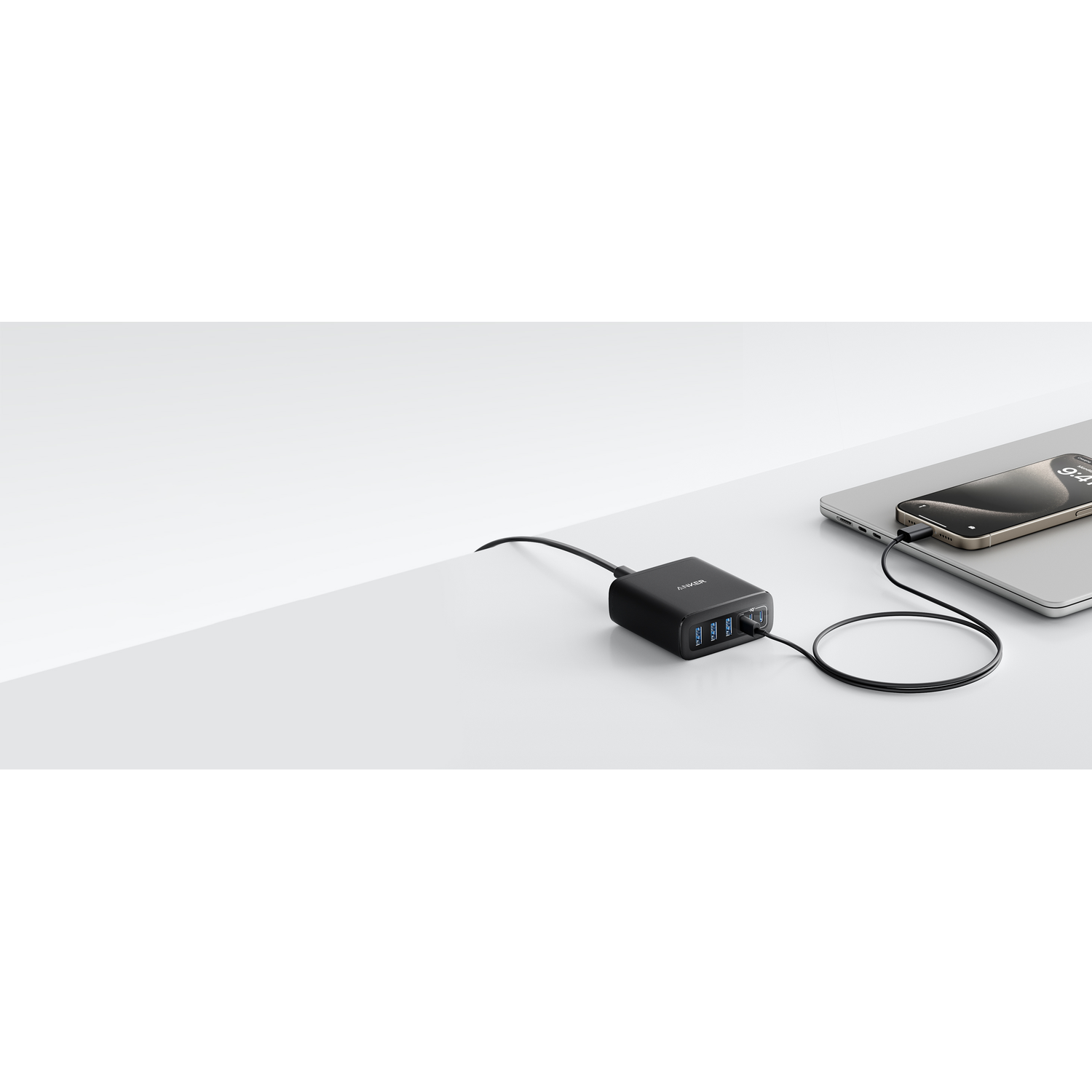 Un chargeur USB Anker noir avec des câbles connectés à un ordinateur portable et un téléphone. Le téléphone est sur le dessus de l'ordinateur portable.