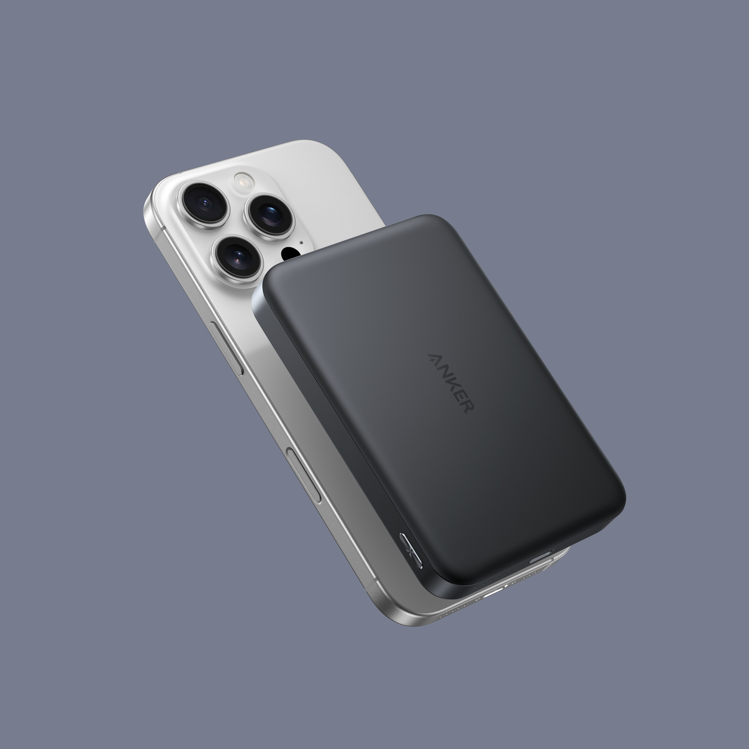 A silver iPhone with a black Anker power bank attached. The phone has three camera lenses. Background is a solid gray.