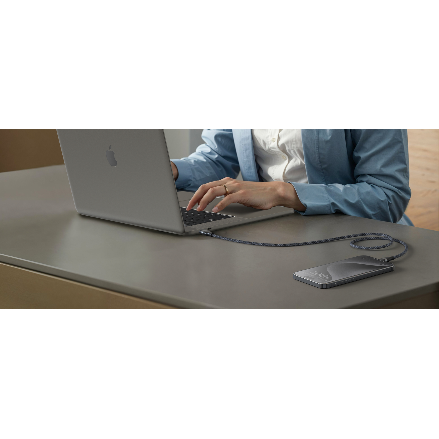Personne utilisant un ordinateur portable, connecté à un téléphone par un câble sur une table. L'ordinateur est argenté, le téléphone noir.
