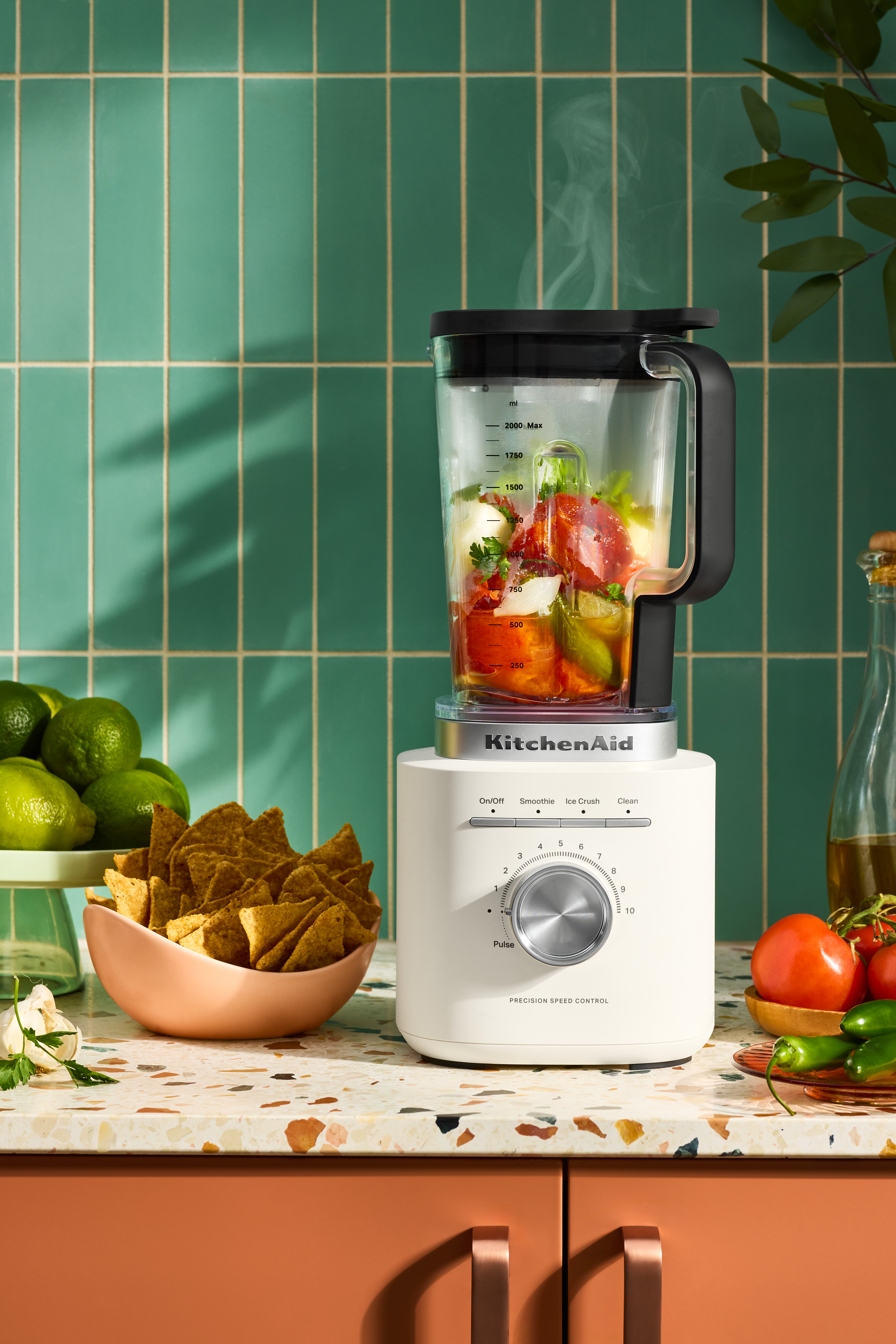 Ein KitchenAid-Mixer mit Essen im Inneren. Limetten, Chips, Tomaten und Paprika sind ebenfalls auf der Theke.