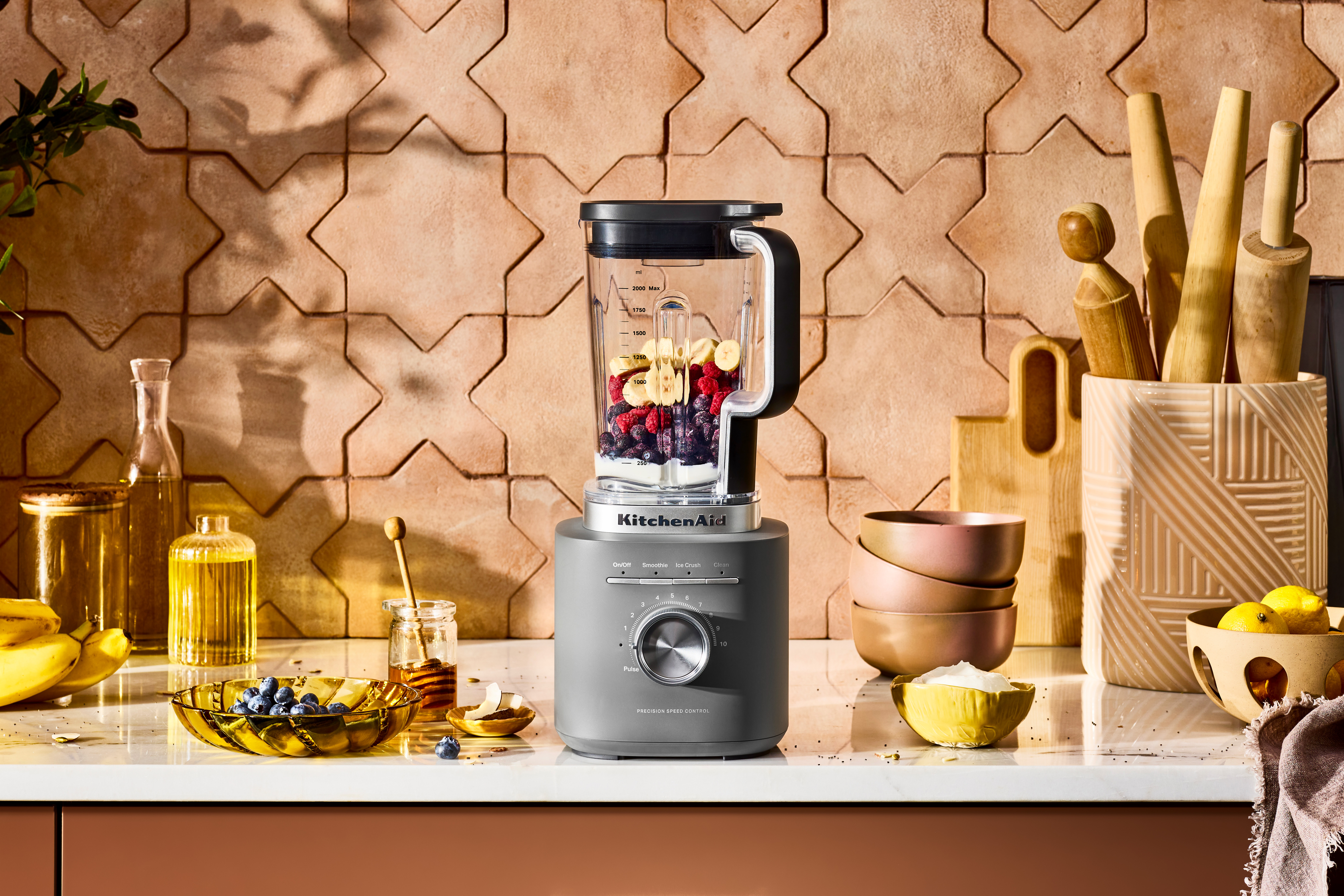Ein KitchenAid-Mixer mit Früchten. Schalen, Honig und Zitronen stehen auf der Theke. Im Hintergrund eine gemusterte Fliesenwand.