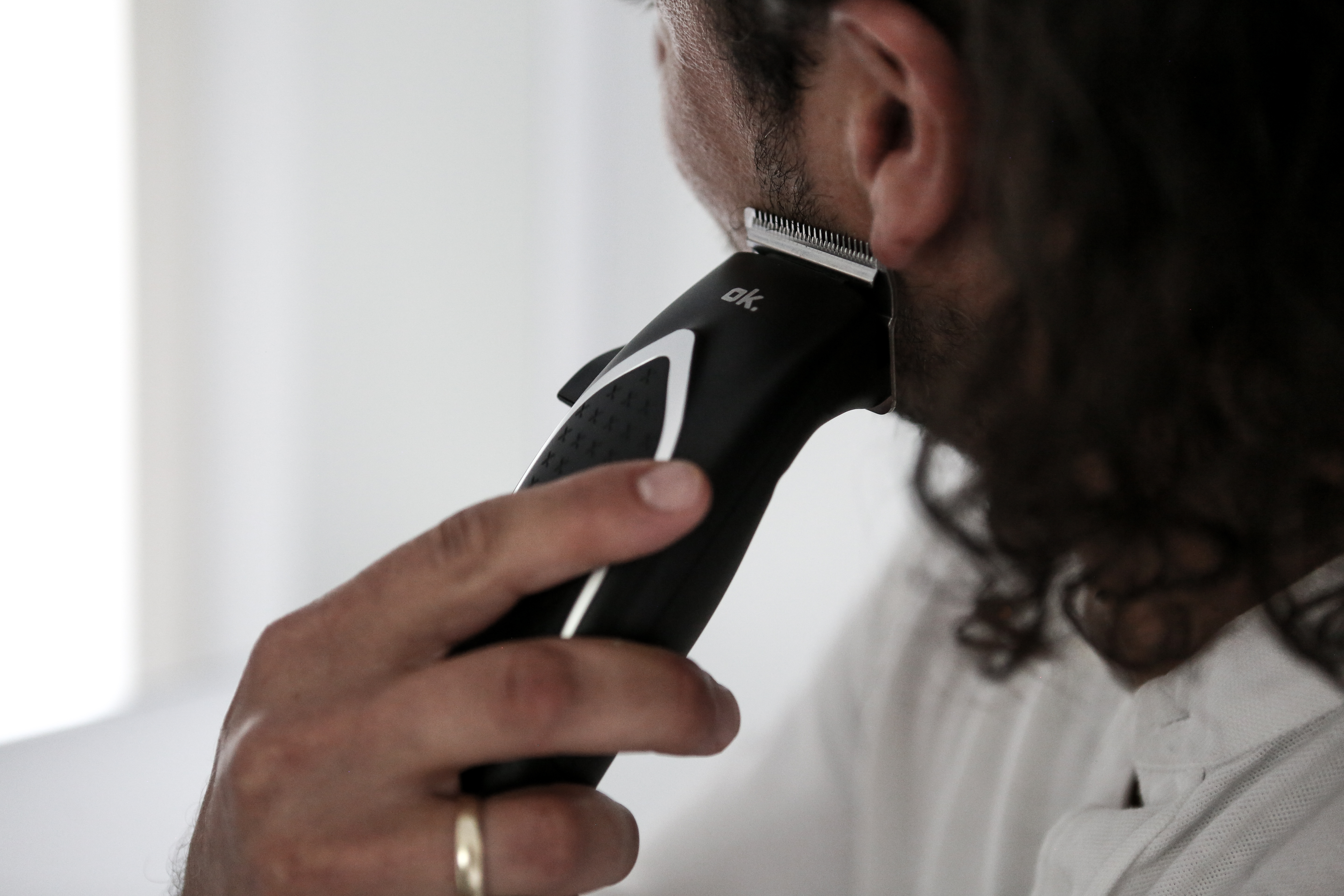 Osoba goli brodę czarno-srebrną golarką elektryczną. Złoty pierścionek jest na palcu.