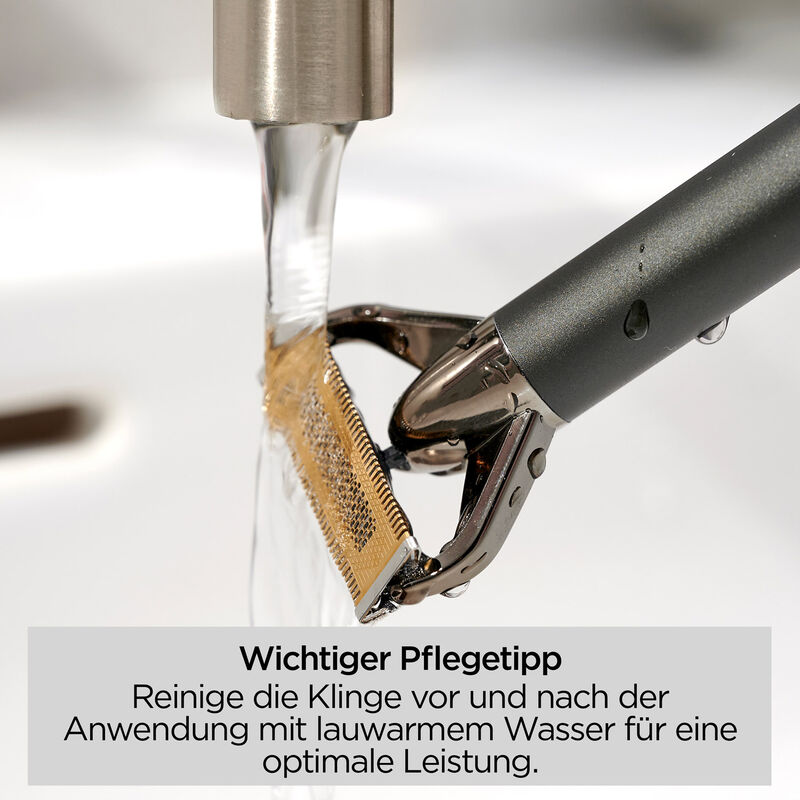 Eine Rasierklinge wird unter fließendem Wasser gespült. Die Klinge ist goldfarben, der Griff dunkelgrau, Wassertropfen sind sichtbar.