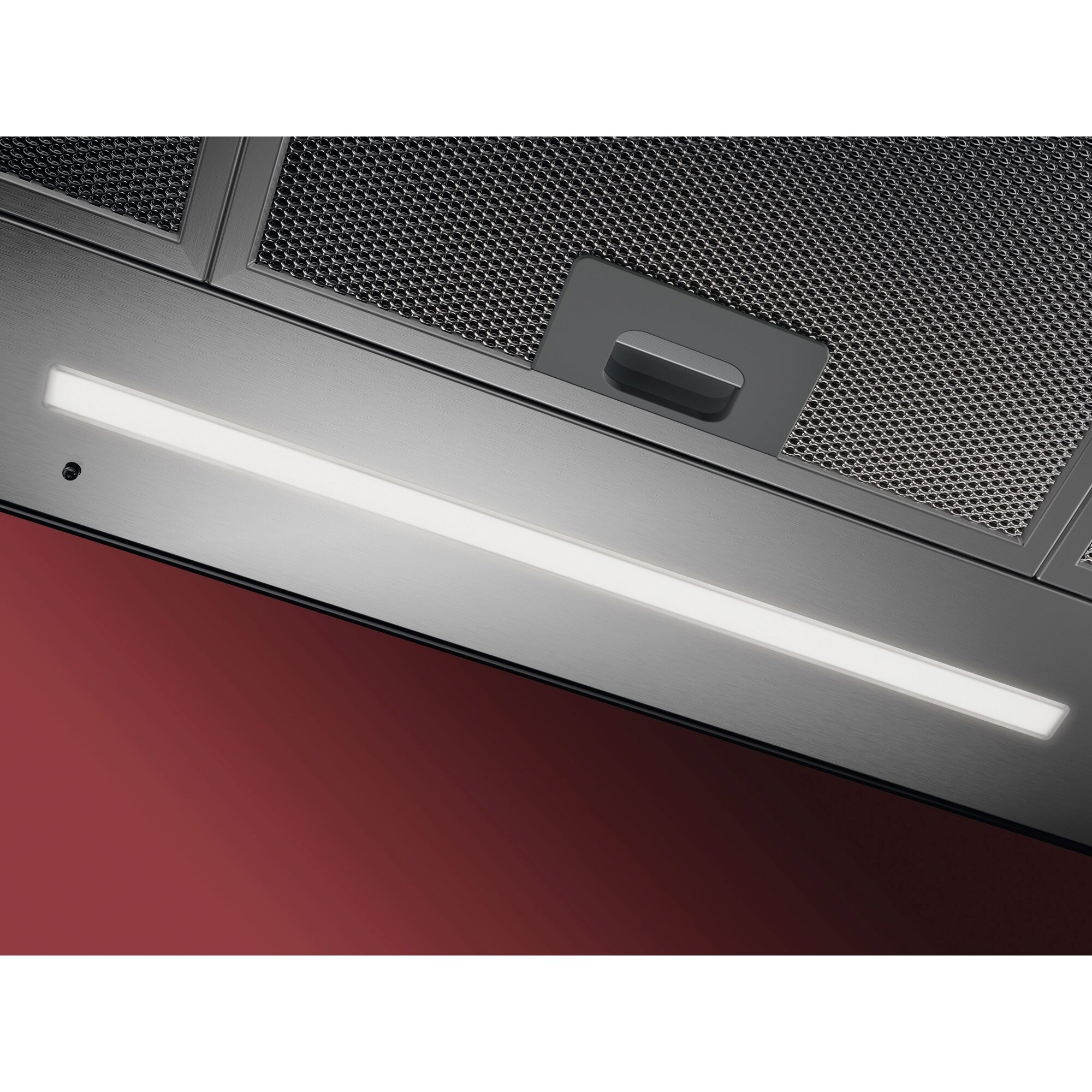 Campana extractora de acero inoxidable con luz brillante. El fondo es una superficie roja.
