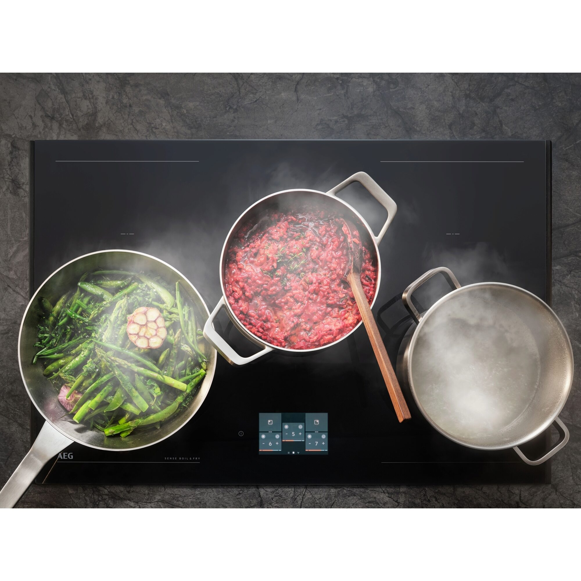 Una placa negra con tres ollas: verduras verdes, risotto rojo y agua hirviendo. Una cuchara de madera en el risotto.