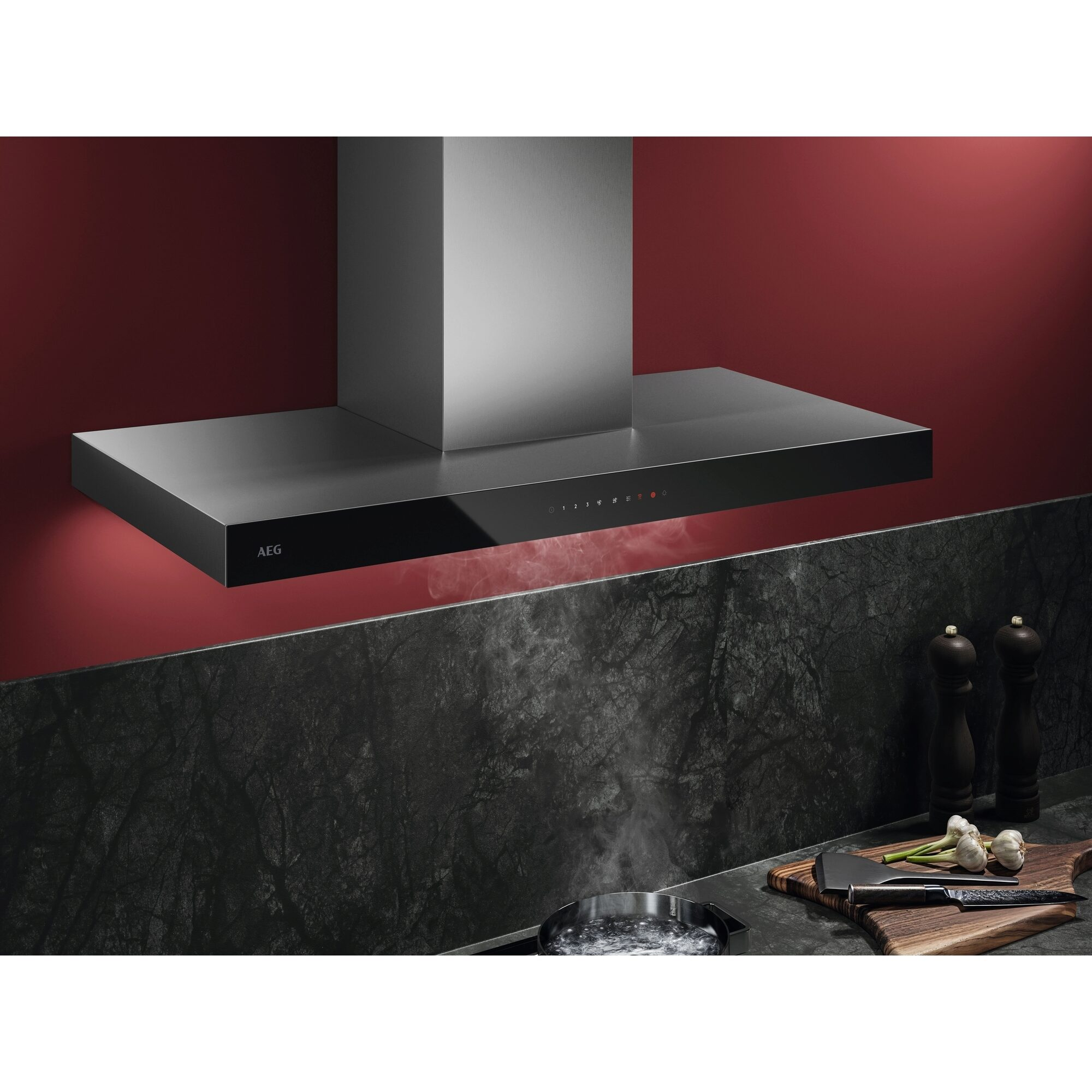 Escena de cocina con campana extractora negra moderna. Primer plano con utensilios de cocina e ingredientes. Pared roja en el fondo.