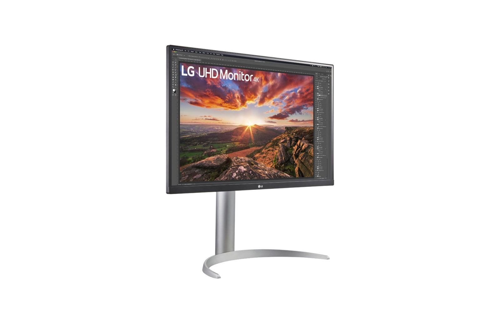 Monitor LG UHD wyświetla zdjęcie krajobrazu. Ma srebrną podstawę. Ekran wyświetla zachód słońca z górami i drzewami.