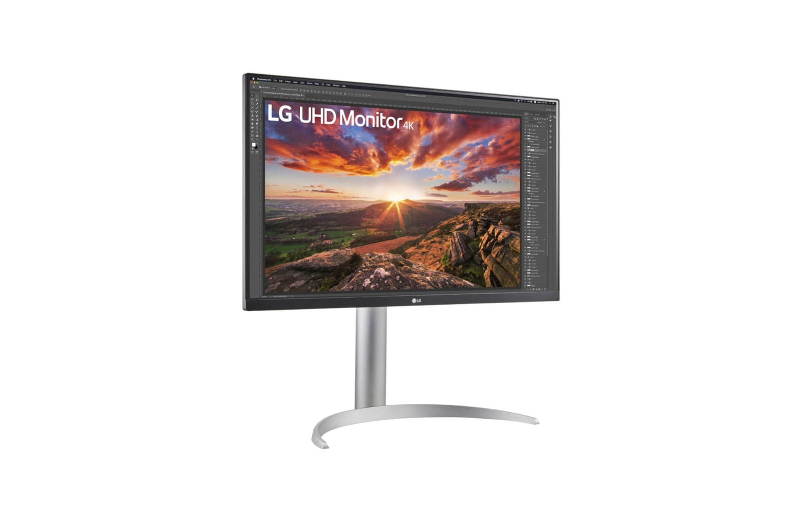 Monitor LG UHD 4K z krajobrazem. Ma srebrną podstawę. Ekran pokazuje zachód słońca nad wzgórzami i skałami.