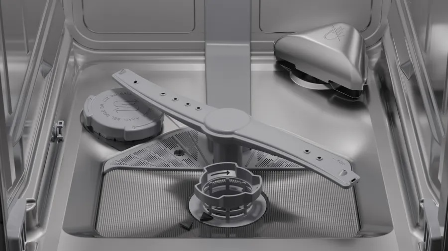 Wnętrze zmywarki. Szare ramię natryskowe, filtr i dozownik detergentu są widoczne. Wnętrze jest metalicznie szare.