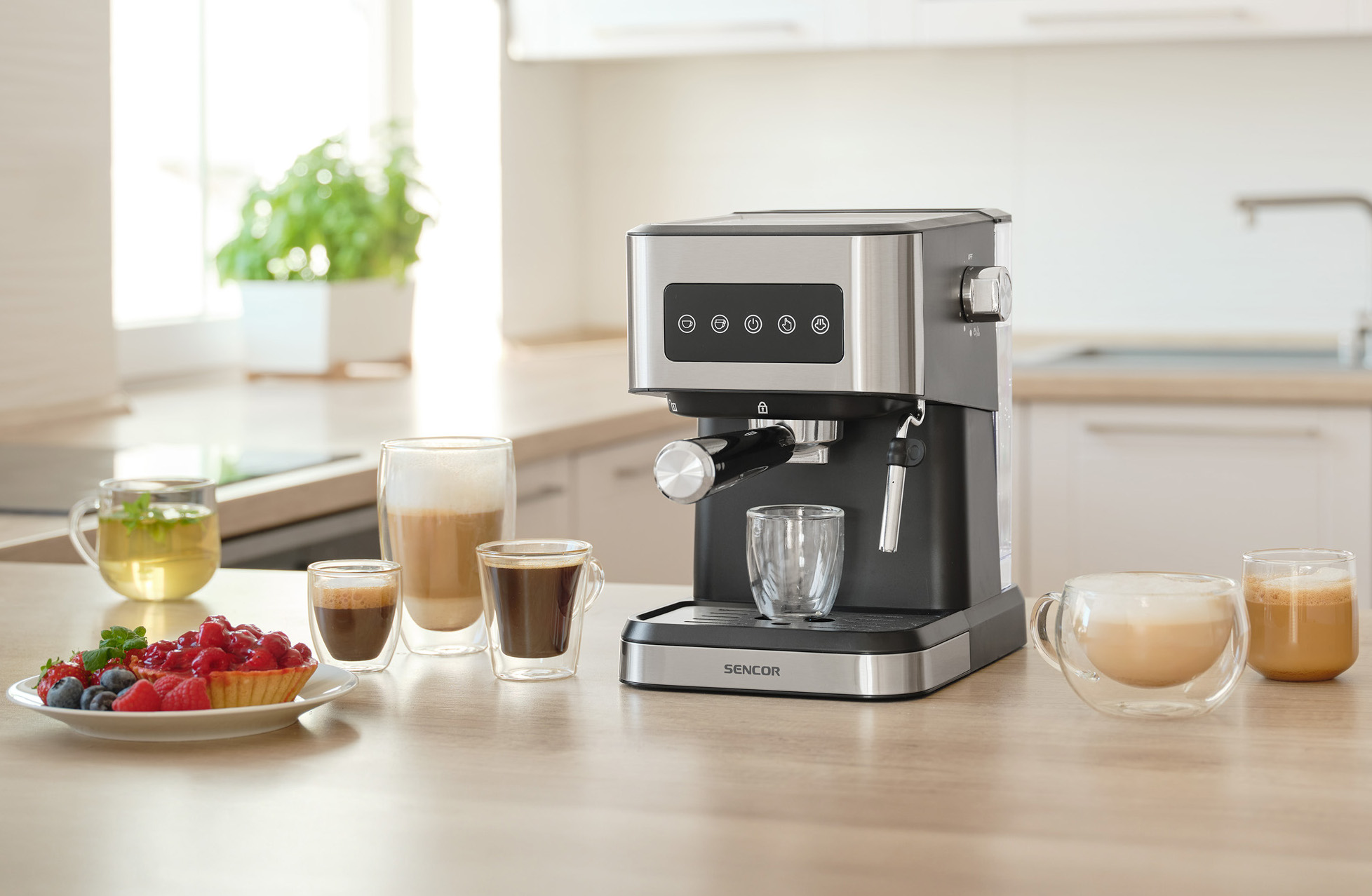 Ekspres do kawy z kawą i ciastkami na drewnianym stole. Tło przedstawia kuchnię z roślinami.