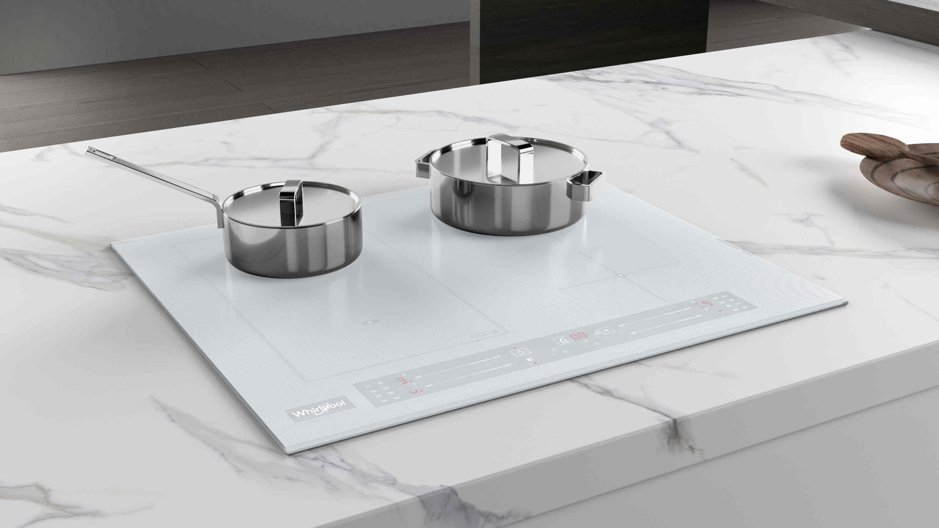 Biała płyta indukcyjna z dwoma garnkami ze stali nierdzewnej na marmurowym blacie. W pobliżu spoczywa drewniana łyżka.