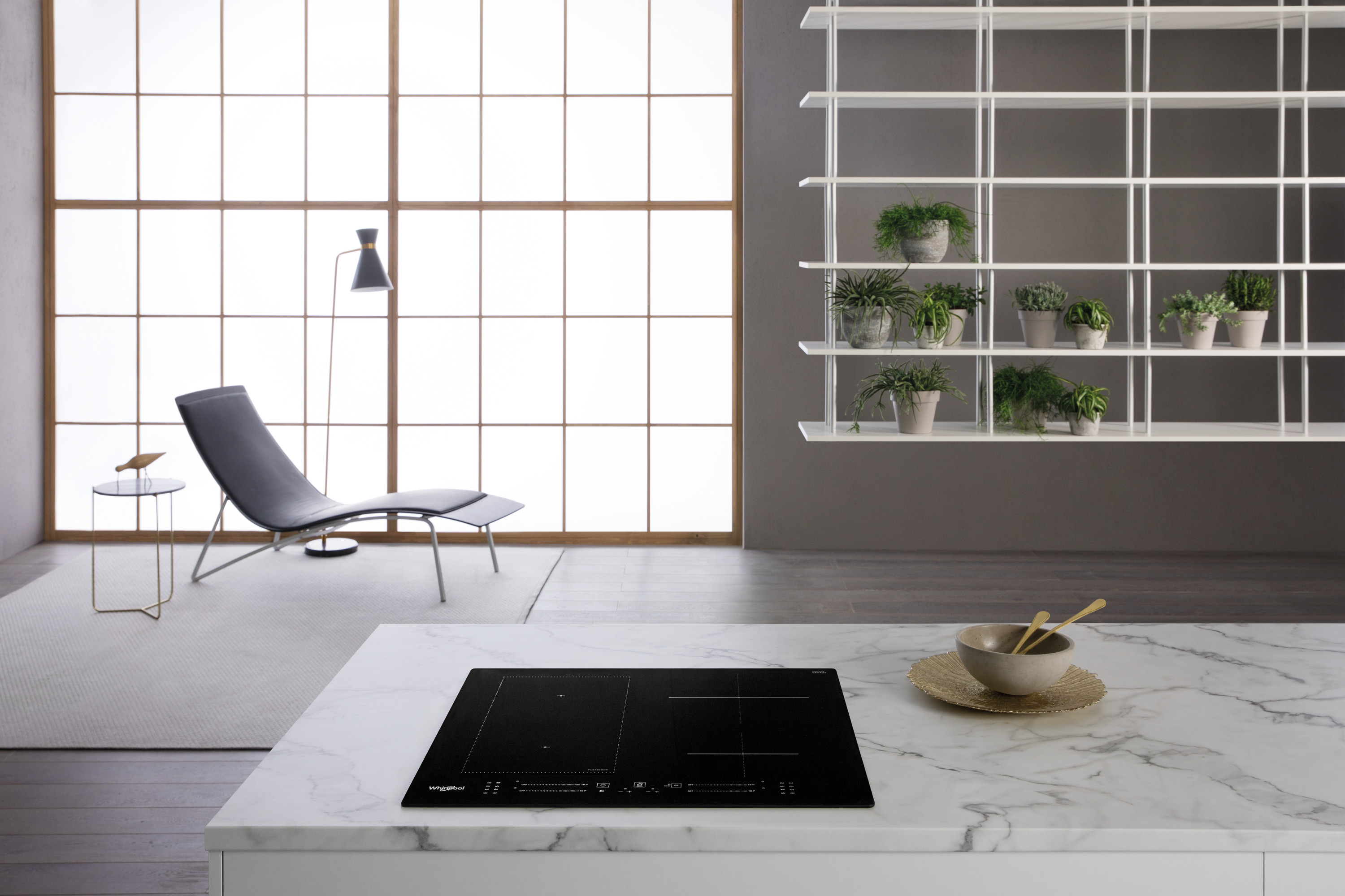 Nowoczesna kuchnia z czarną płytą grzewczą, marmurowym blatem i szarym krzesłem. Okno i półka z roślinami w tle.