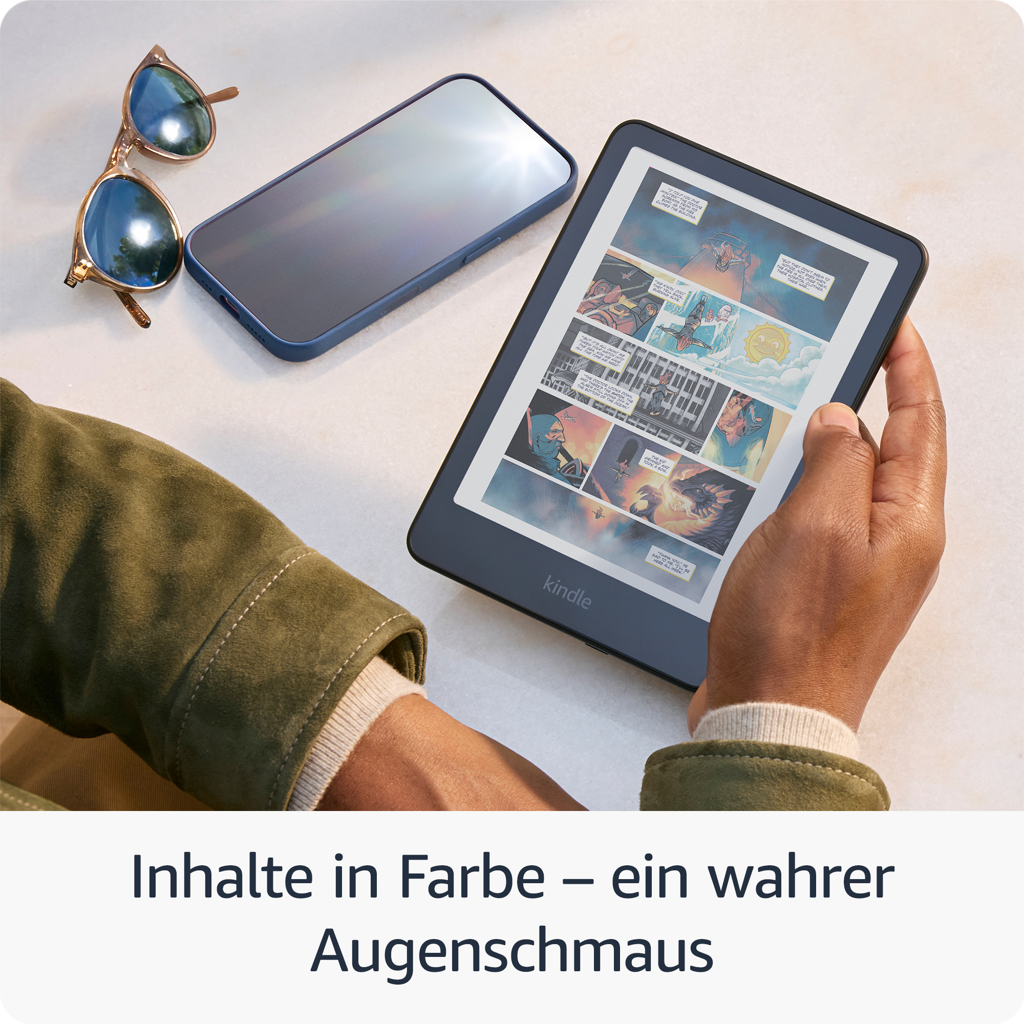 Eine Person hält einen Kindle mit einem Comic. Sonnenbrille und Telefon liegen daneben auf einer hellen Oberfläche.