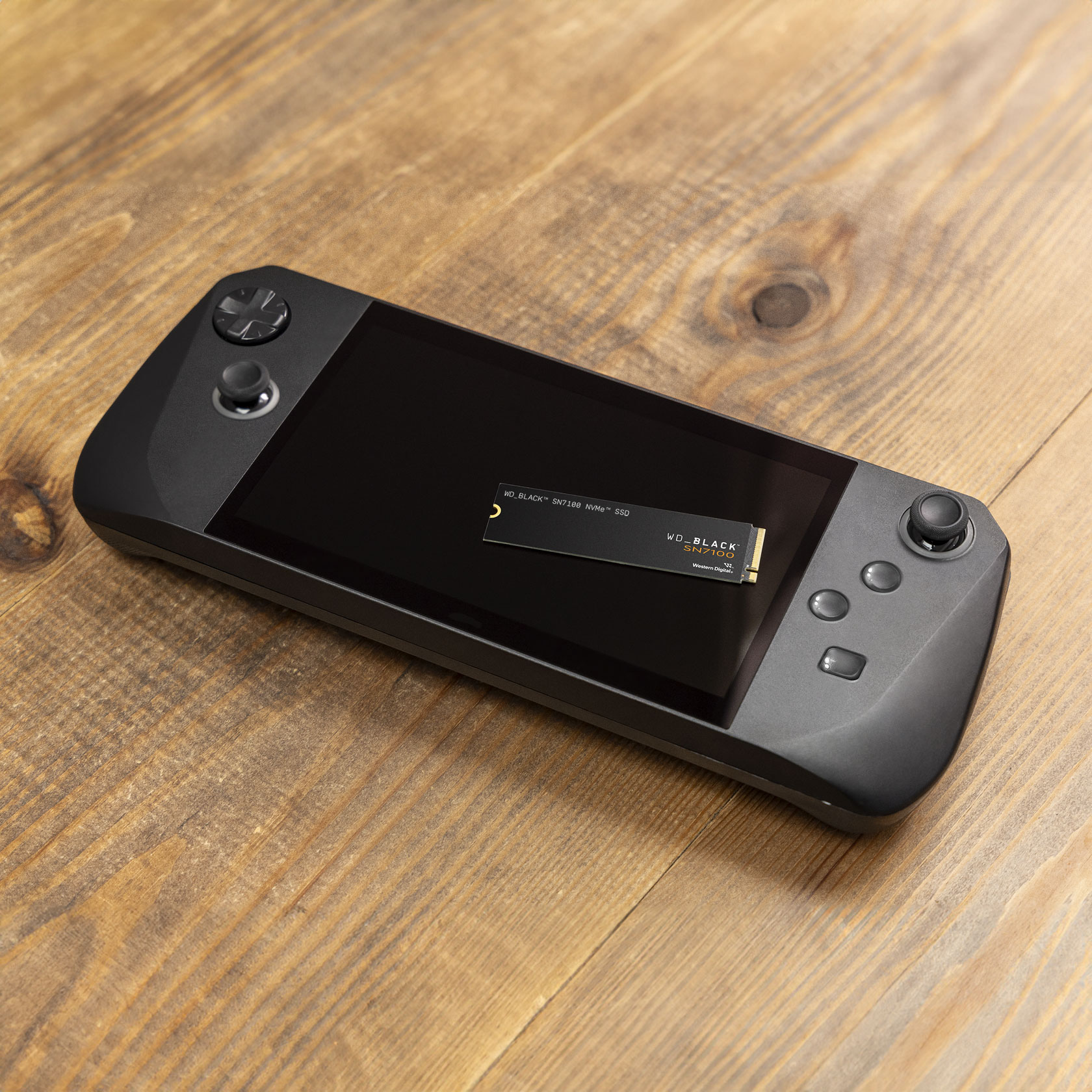 Eine schwarze Handheld-Spielekonsole mit Bildschirm, mit einer WD_BLACK SN7100 SSD auf dem Bildschirm, auf einer Holzoberfläche.