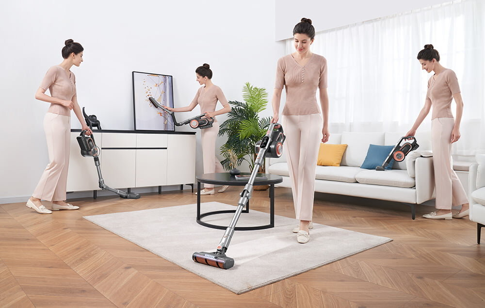 Kobieta używa odkurzacza w salonie. Ma na sobie jasnoróżowy strój. Pokój ma białą sofę, dywan i drewnianą podłogę.