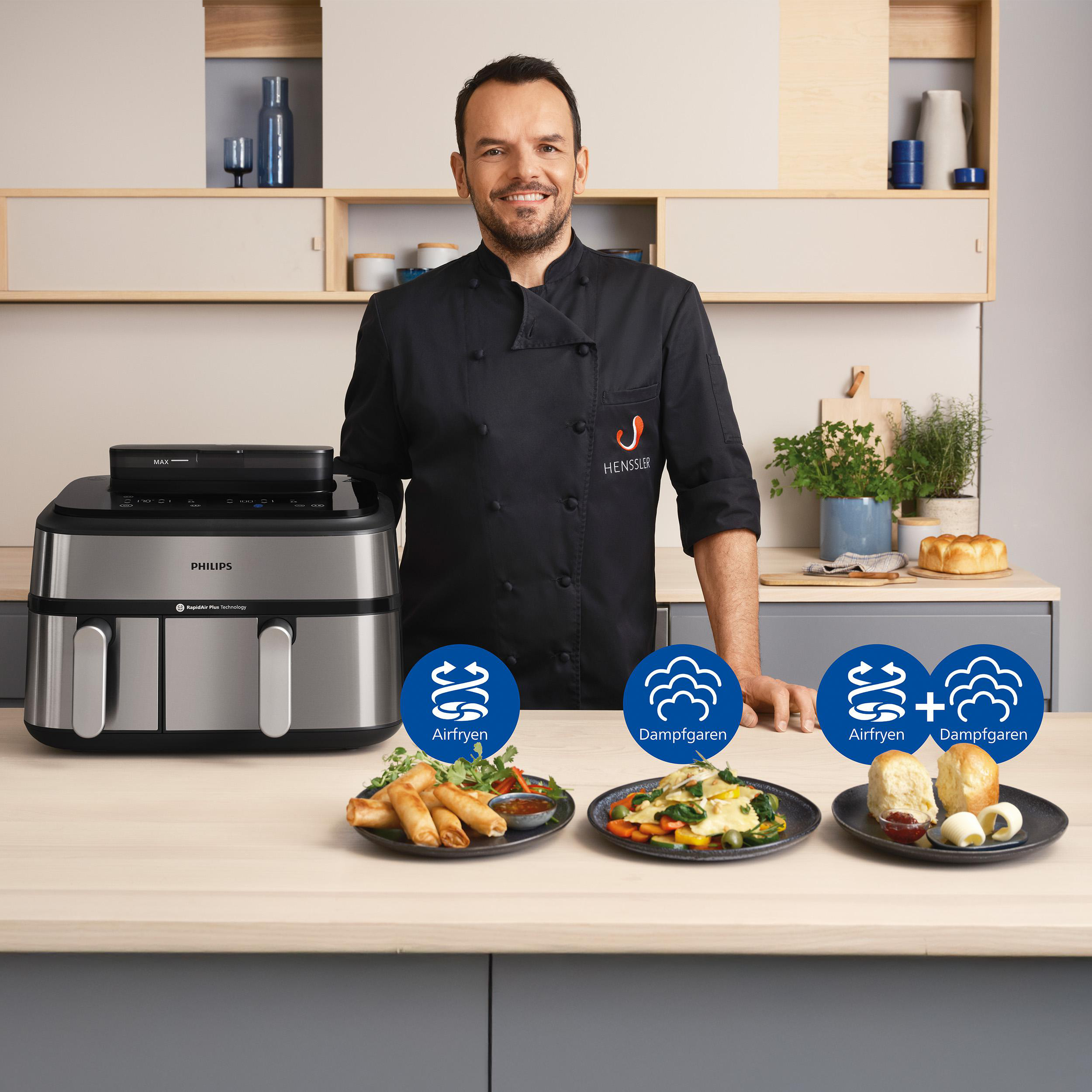 Koch in schwarzem Mantel mit Philips-Heißluftfritteuse und Gerichten auf der Theke. Mit Airfryen, Dampfgaren Symbolen.