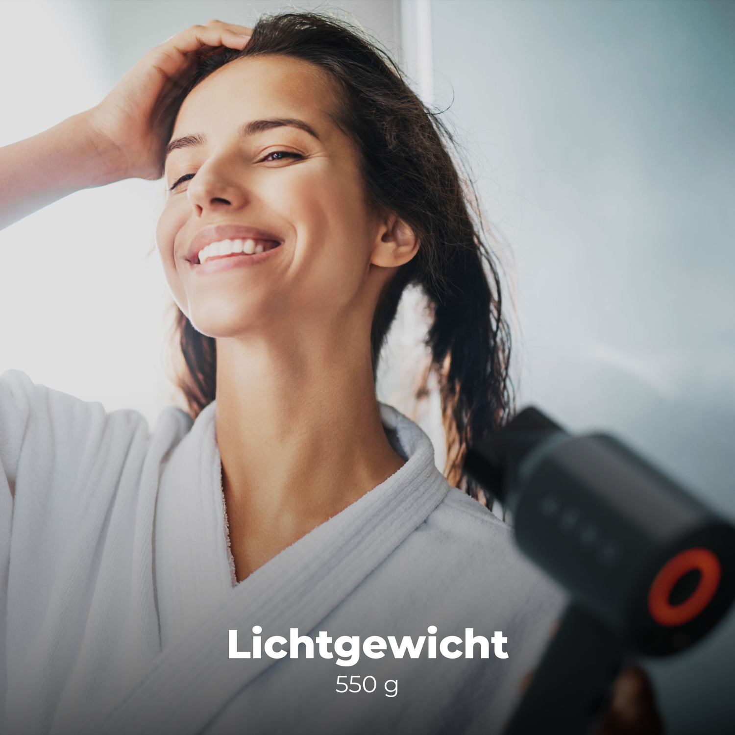 Een vrouw glimlacht, raakt haar natte haar aan. Ze draagt een witte badjas en houdt een zwarte föhn vast. Tekst: Lichtgewicht 550 g.