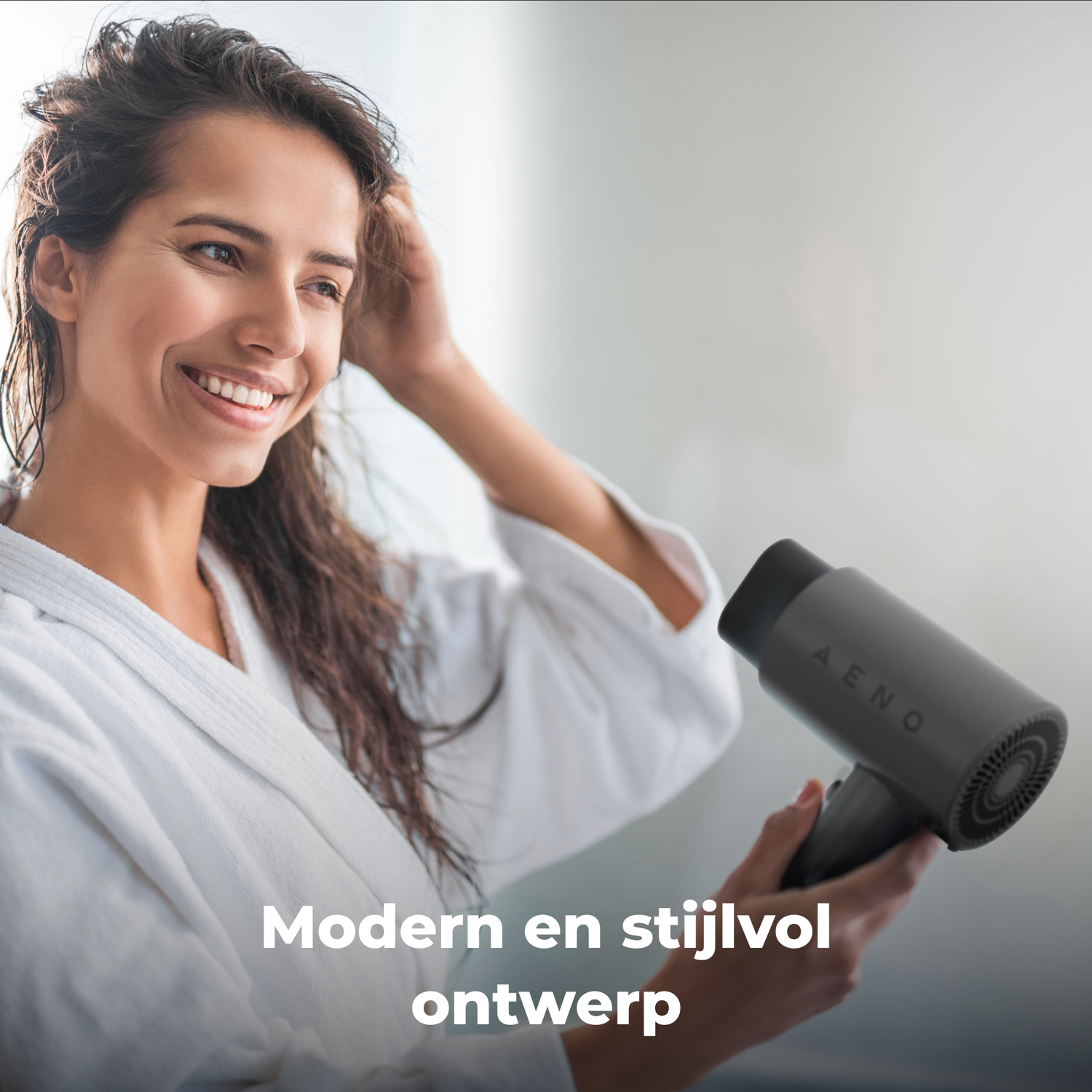 Woman smiles, holding wet hair and a gray hairdryer. She wears a white robe. The background is blurred.