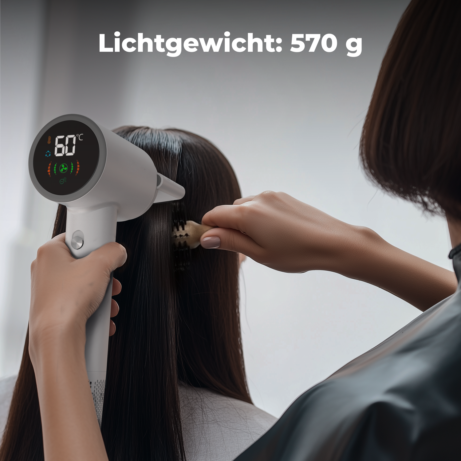 A person is using a hairdryer on another person's hair. The hairdryer shows 60°C. The background is a neutral color.