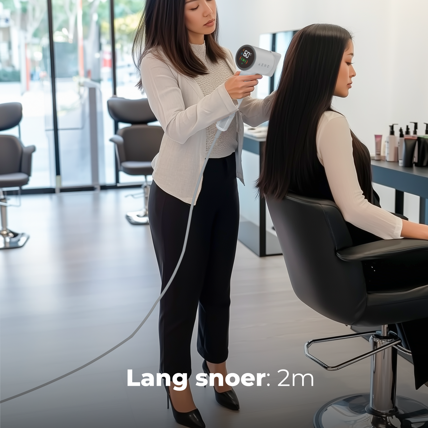A woman is drying another woman's hair with a white hairdryer in a salon. The hair is long and black. The cord is 2m.