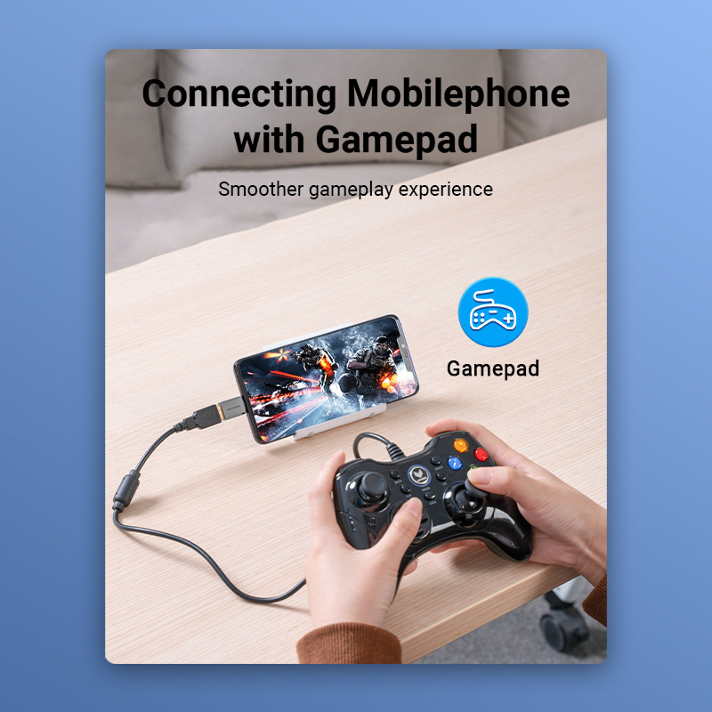 Egy telefon egy gamepadhoz van csatlakoztatva. A telefon egy játékot mutat. Egy személy tartja a gamepadot. A háttérben szöveg van.