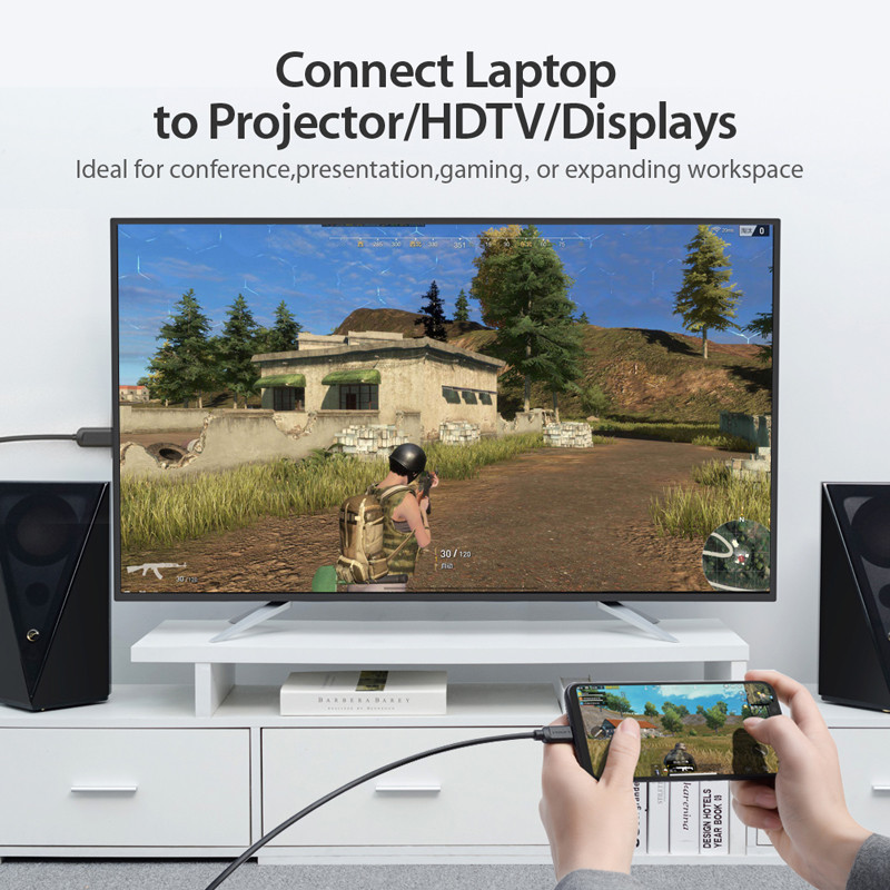 Egy képernyő egy játékot mutat. Egy telefon ugyanazt a játékot mutatja, kábellel csatlakoztatva. Hangszórók mindkét oldalon. Szöveg: Laptop csatlakoztatása projektorhoz.