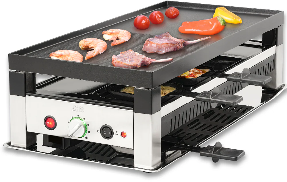 Ein Raclette-Grill mit Essen oben: Garnelen, Fleisch und Gemüse. Darunter Käsepfannen. Der Grill hat Knöpfe und ein rotes Licht.