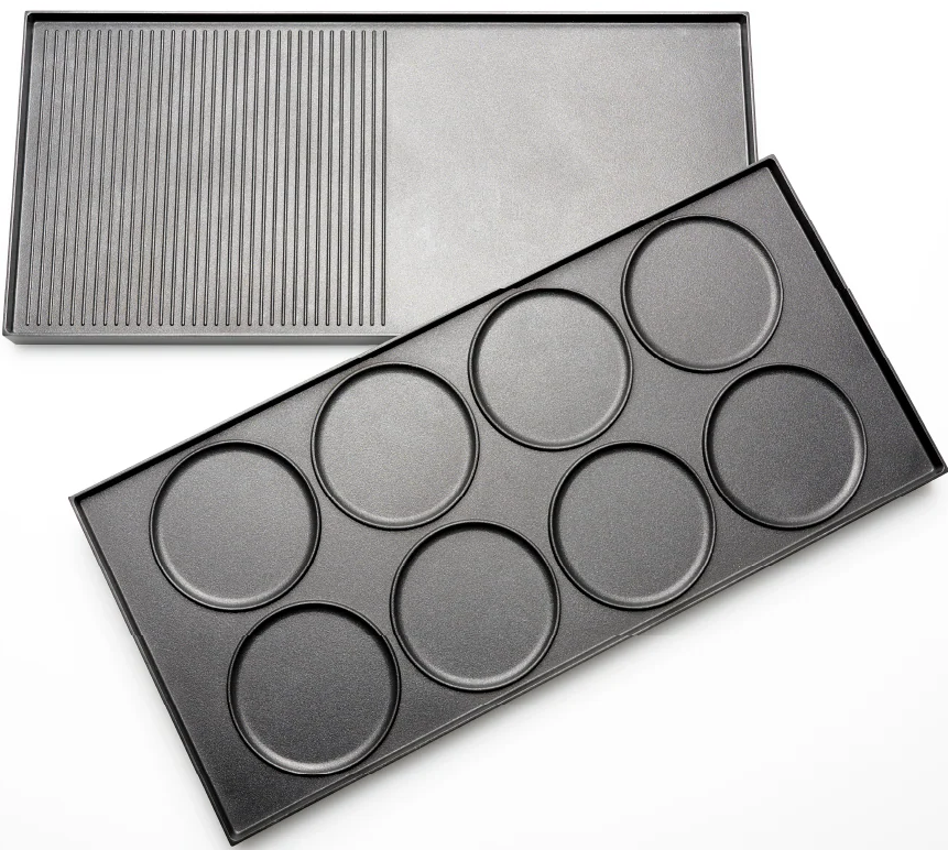 Zwei schwarze Metallbackbleche. Eines mit Grillspuren, das andere mit acht kreisförmigen Vertiefungen für einzelne Kuchen oder Pfannkuchen.