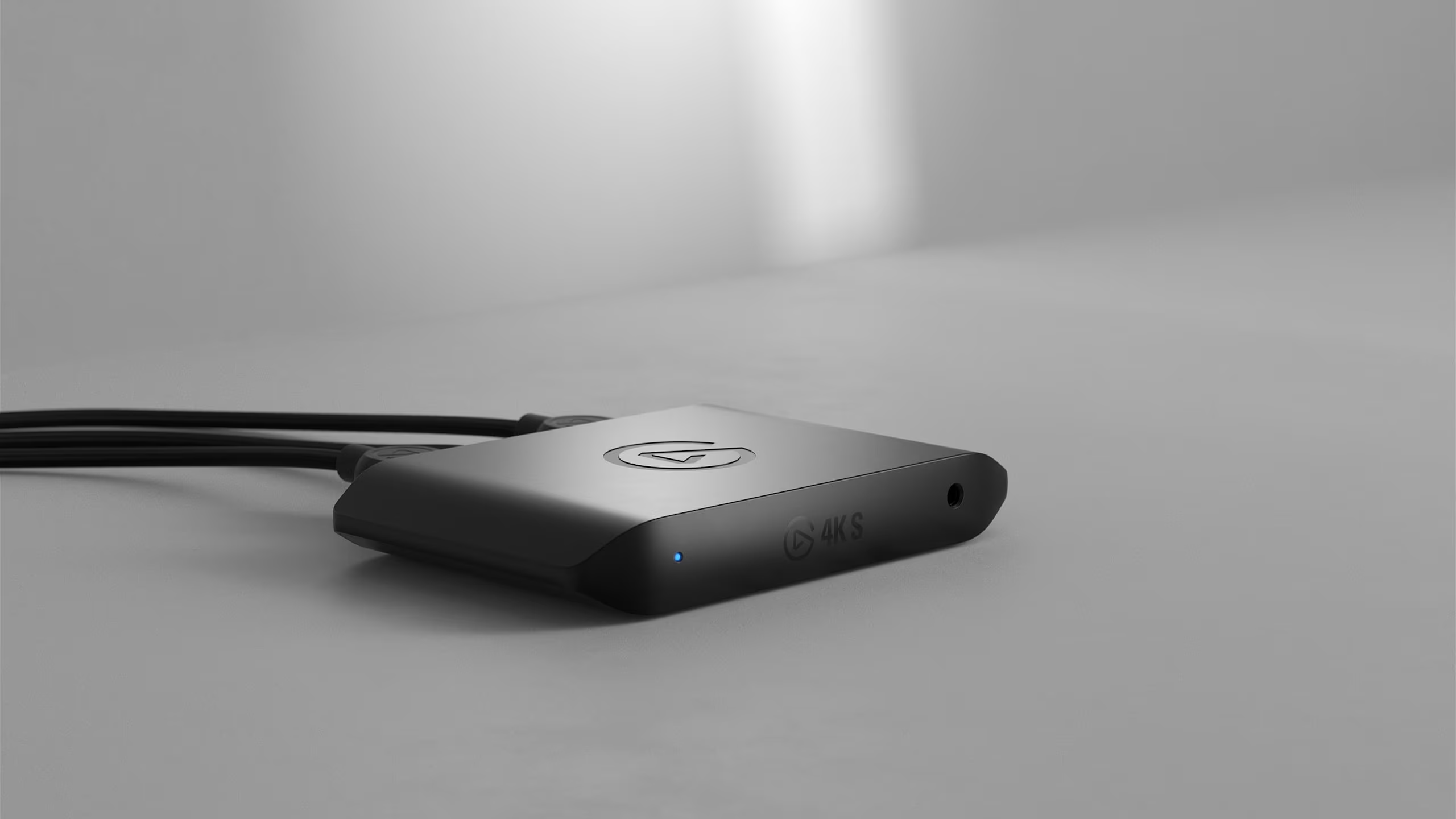 Ein schwarzes Gerät mit Kabeln liegt auf einer grauen Oberfläche. Das Gerät hat ein Logo und ein blaues Licht.