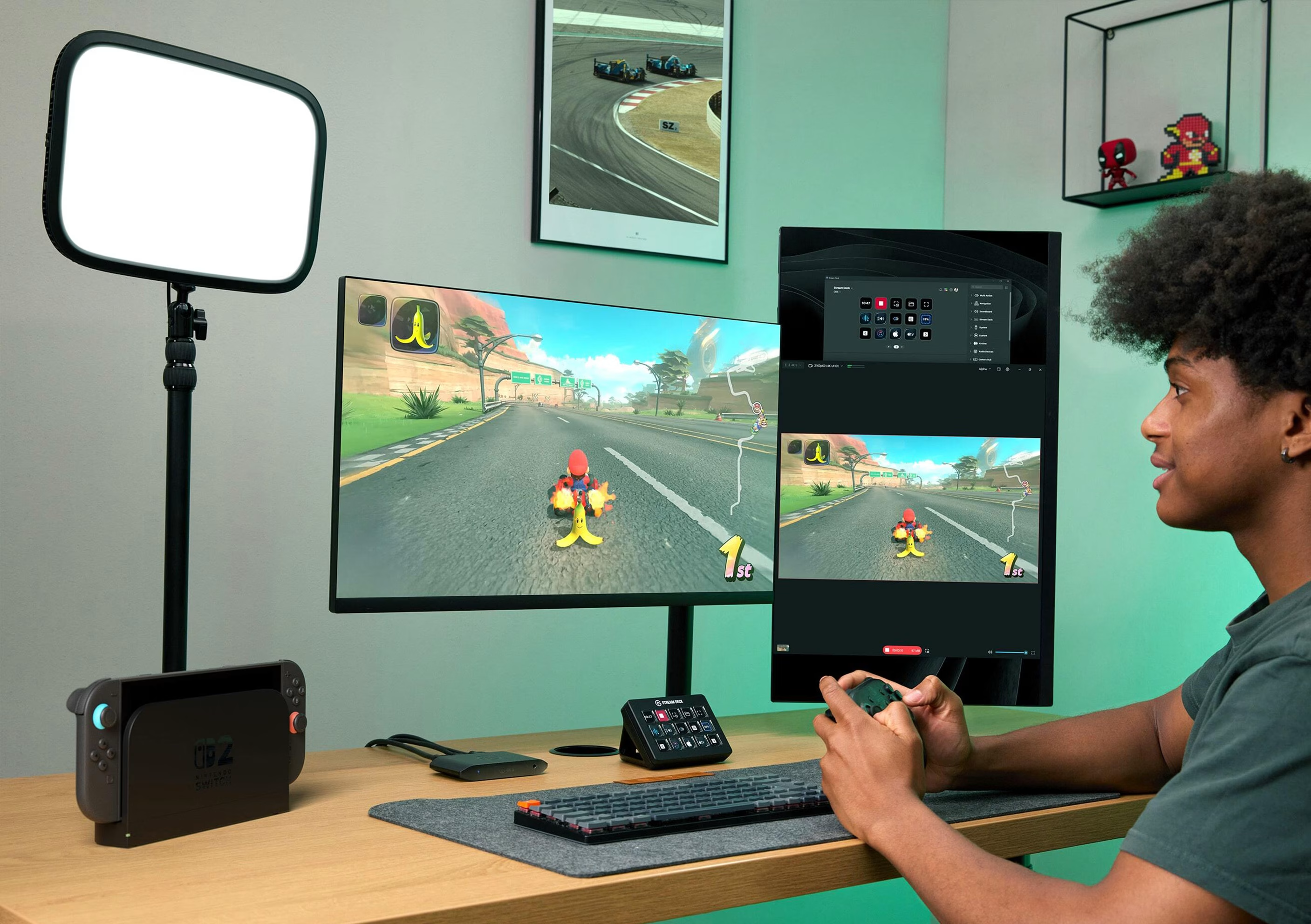 Eine Person spielt ein Rennspiel auf einem Monitor. Ein Licht, eine Konsole und eine Tastatur sind im Bild. Die Person hält einen Controller.
