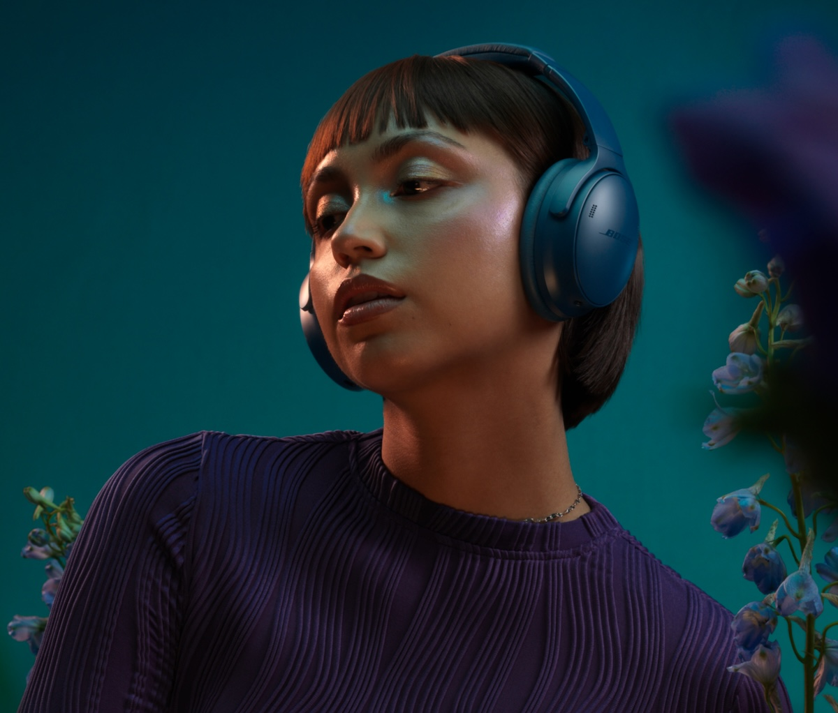 Une femme portant un casque bleu. Elle a les cheveux bruns courts et porte une chemise violette. Des fleurs bleues en arrière-plan.
