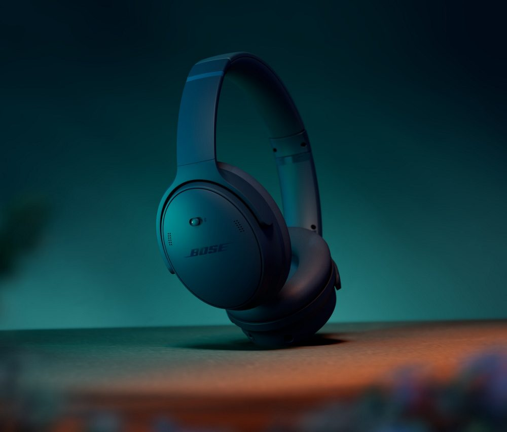 Casque Bose bleu foncé sur une table. Le fond est turquoise et orange. Le casque est l'élément principal.