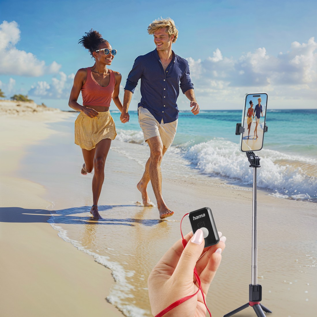 Ein Paar rennt am Strand und hält Händchen. Ein Handy auf einem Stativ nimmt sie auf. Eine Hand hält eine schwarze Fernbedienung mit rotem Kabel.