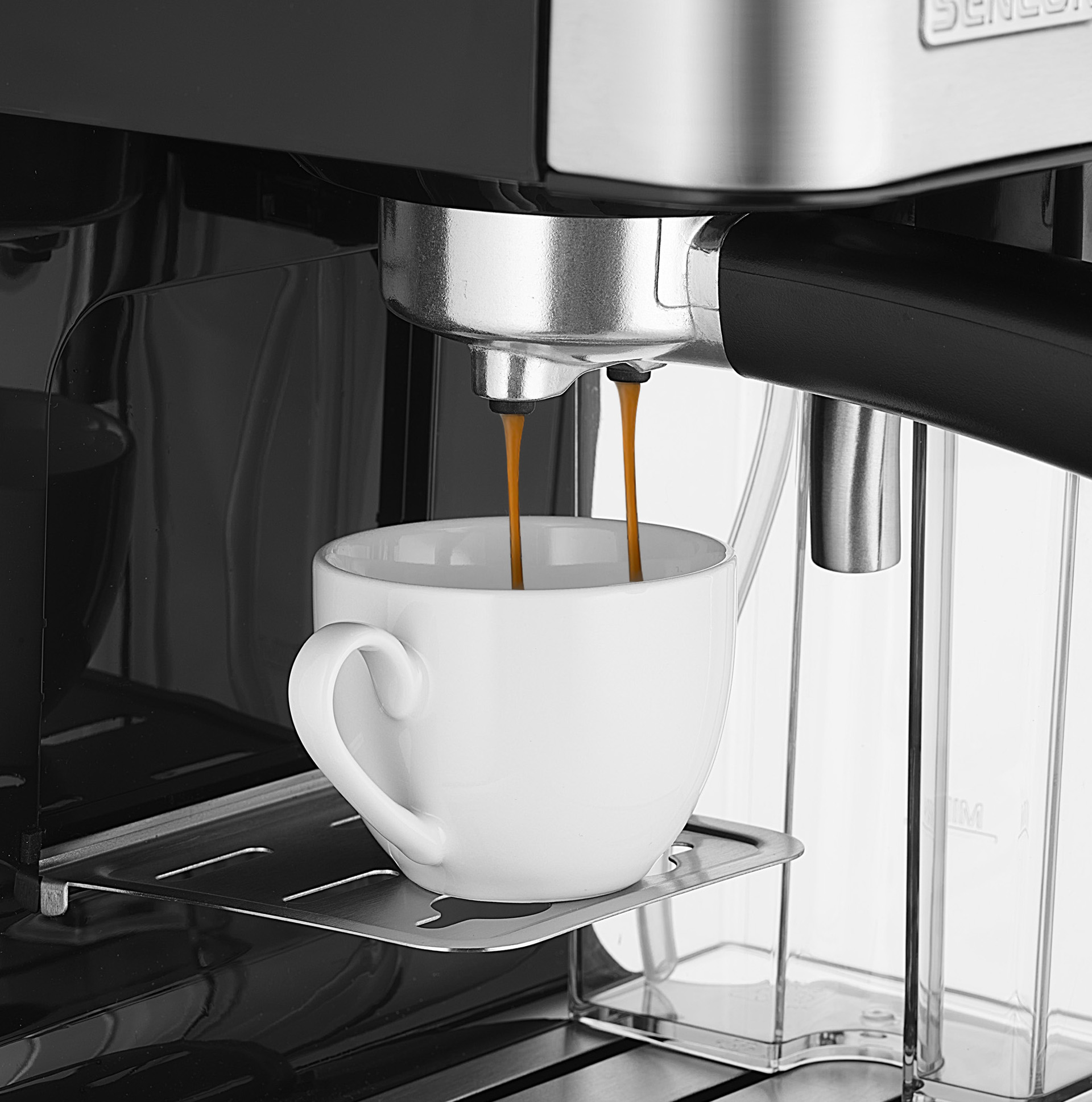 Ekspres do kawy dozujący kawę do białej filiżanki. Maszyna jest czarna i srebrna. Kawa jest ciemnobrązowa.